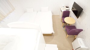 A hotel room with a bed, a desk with a chair, a small round table with a chair, a TV mounted on the wall, and an air conditioning unit. - CVS Bay Hotel Annex (Ichikawa)