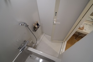 A bathroom with a bathtub, shower, and a shelf with toiletries. - CVS Bay Hotel Annex (Ichikawa)