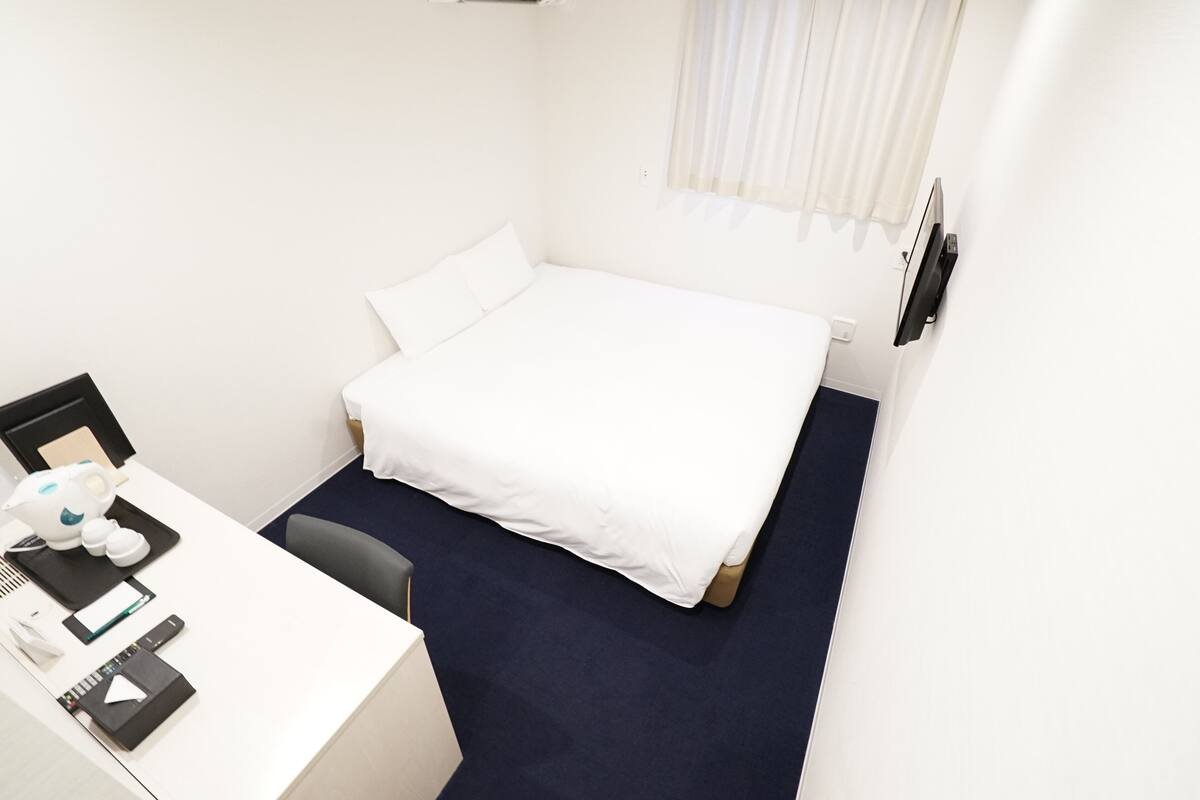 Hotellihuone, jossa on sänky, työpöytä tuolilla ja ikkuna, jossa on verhot.