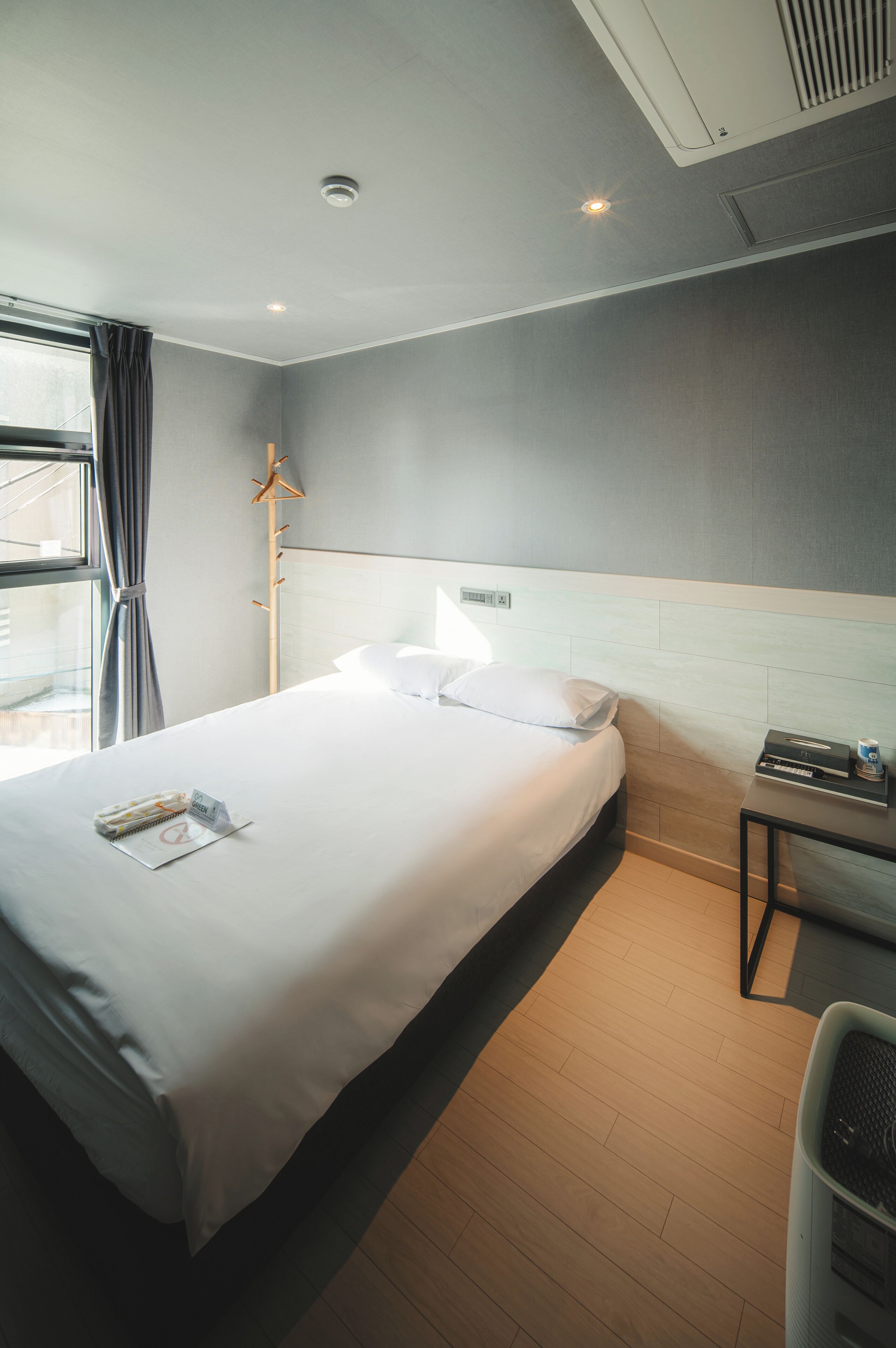A modern hotel room with a large bed, a bedside table, a lamp, and a window with curtains.