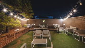 Ein Terrassenbereich im Freien mit Backsteinmauern, grünem Kunstgrün und verschiedenen Sitzgelegenheiten, darunter Tische und Stühle.