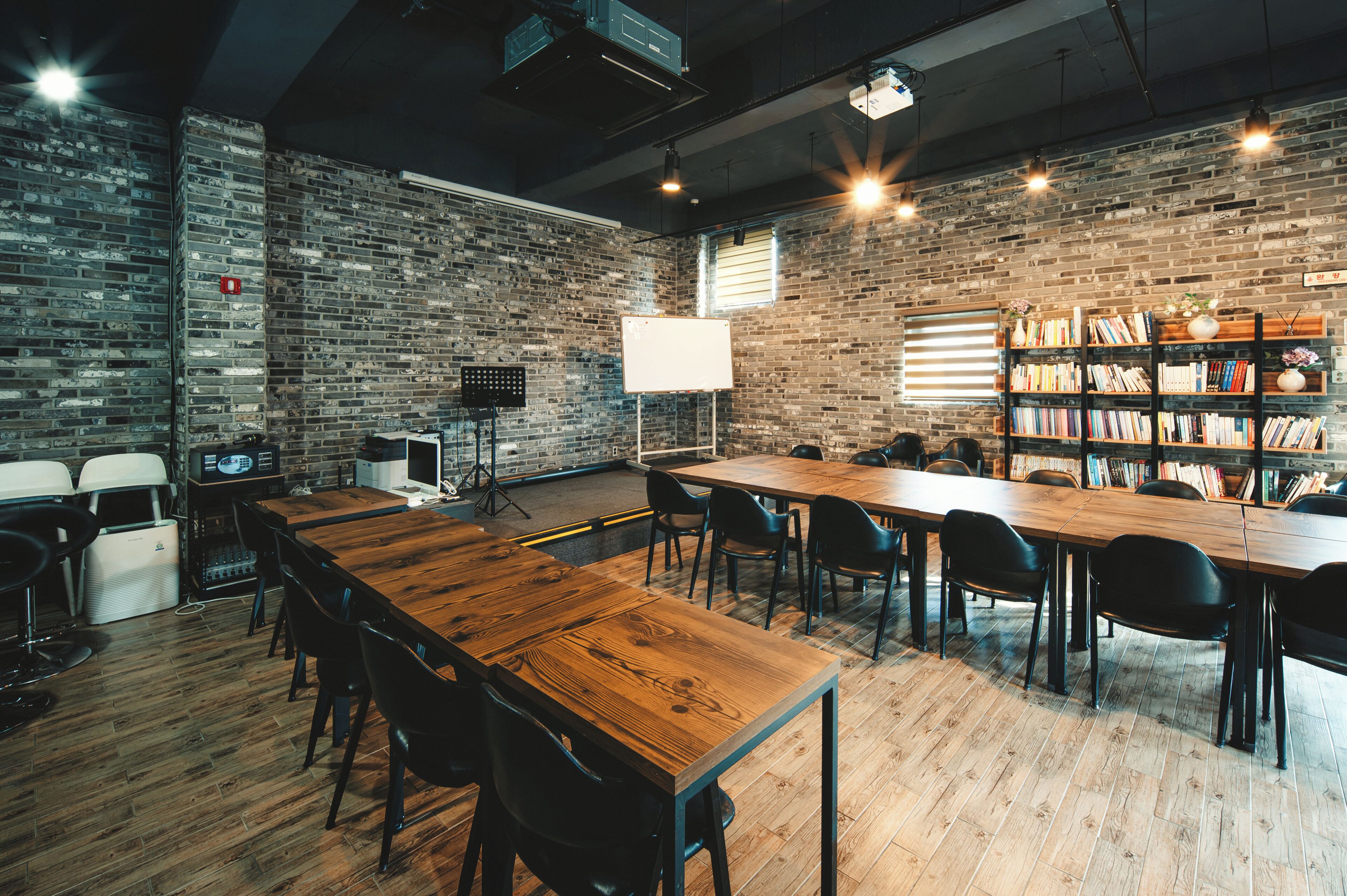 Una sala conferenze con un lungo tavolo di legno, sedie nere, un proiettore, una lavagna e una libreria piena di libri.