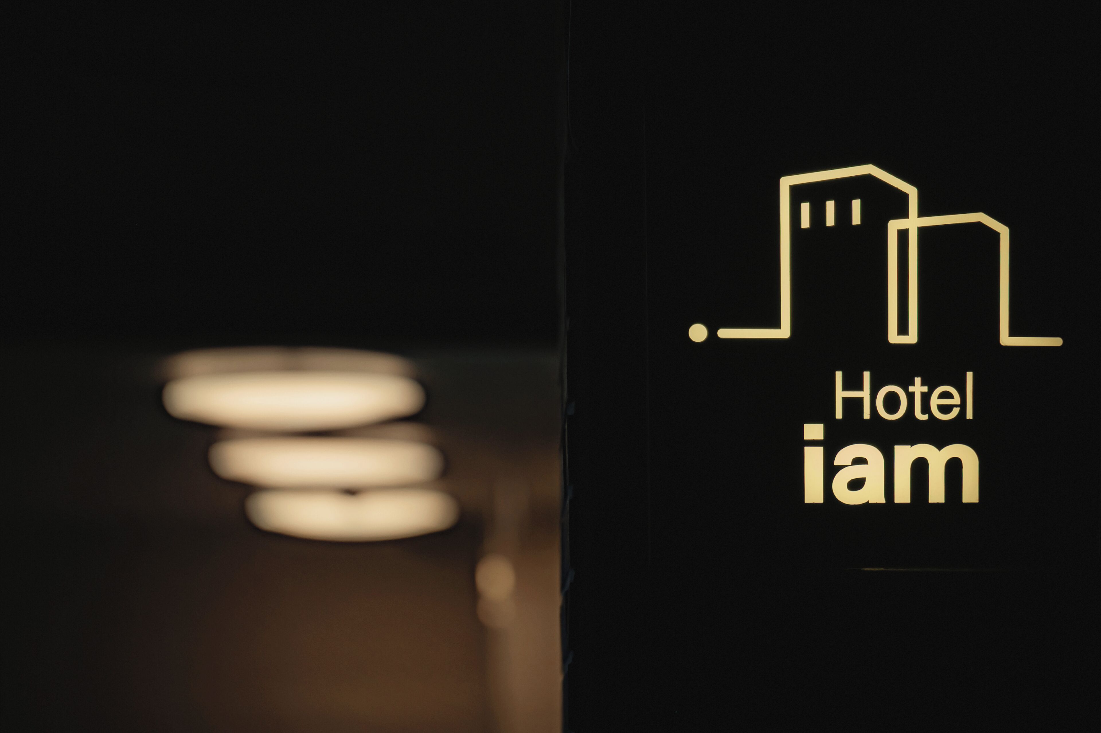 A hotel sign with a minimalist design, featuring a stylized building icon and the text "Hotel iam".