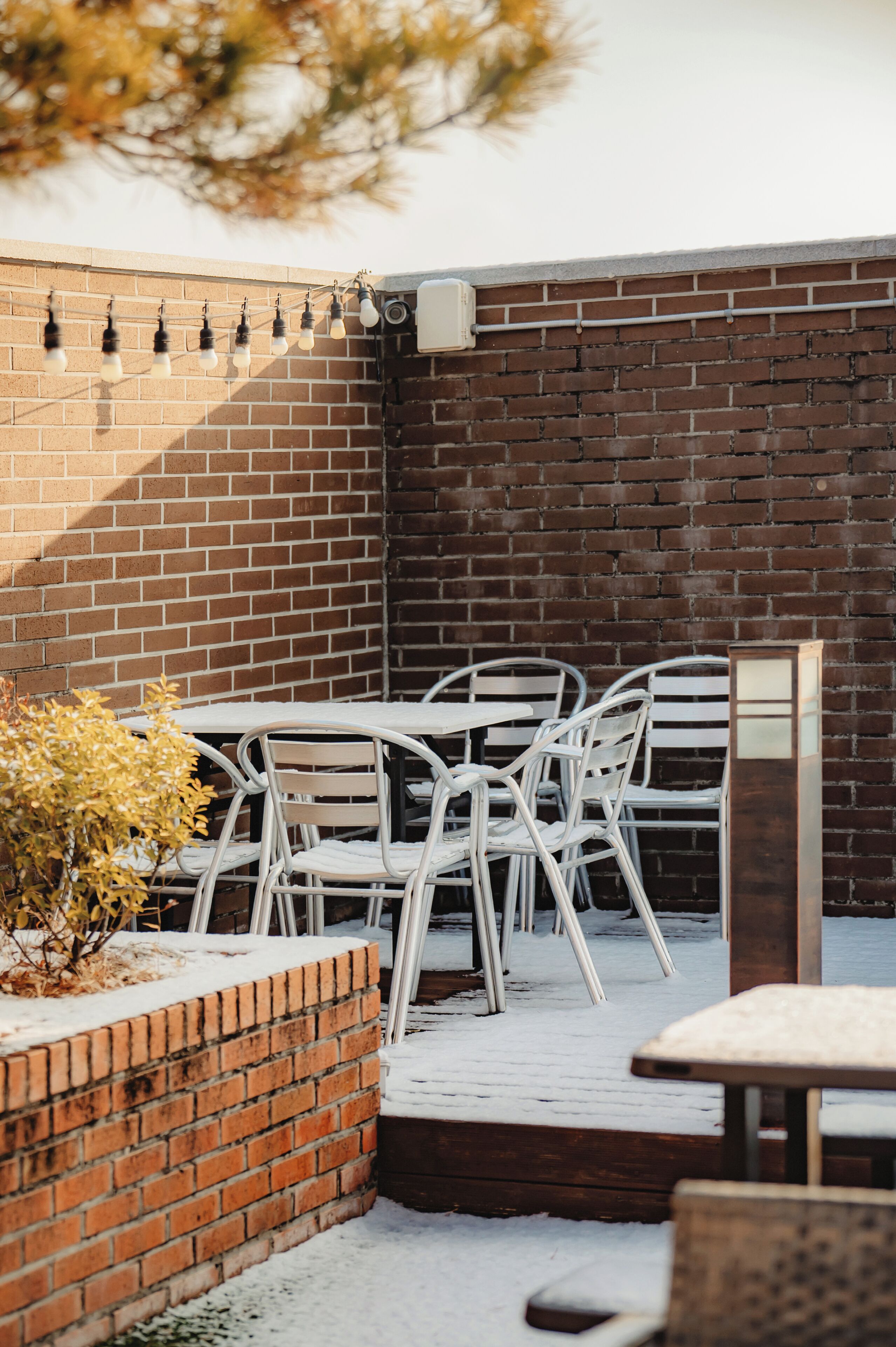 A patio area with a brick wall, white metal chairs, and a table.