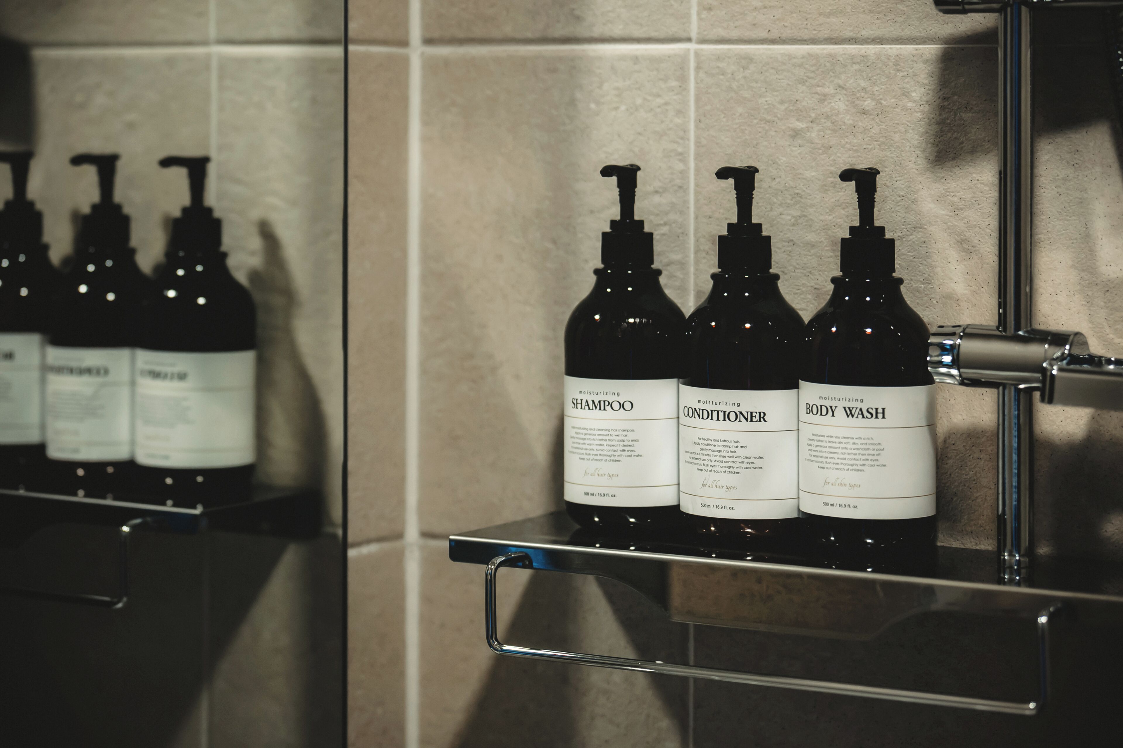 A bathroom shelf with three bottles of body wash and shampoo.