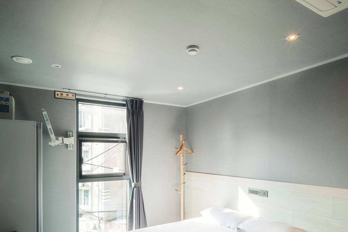 A hotel room with a large bed, a bedside table, a window with curtains, and a view of the city.