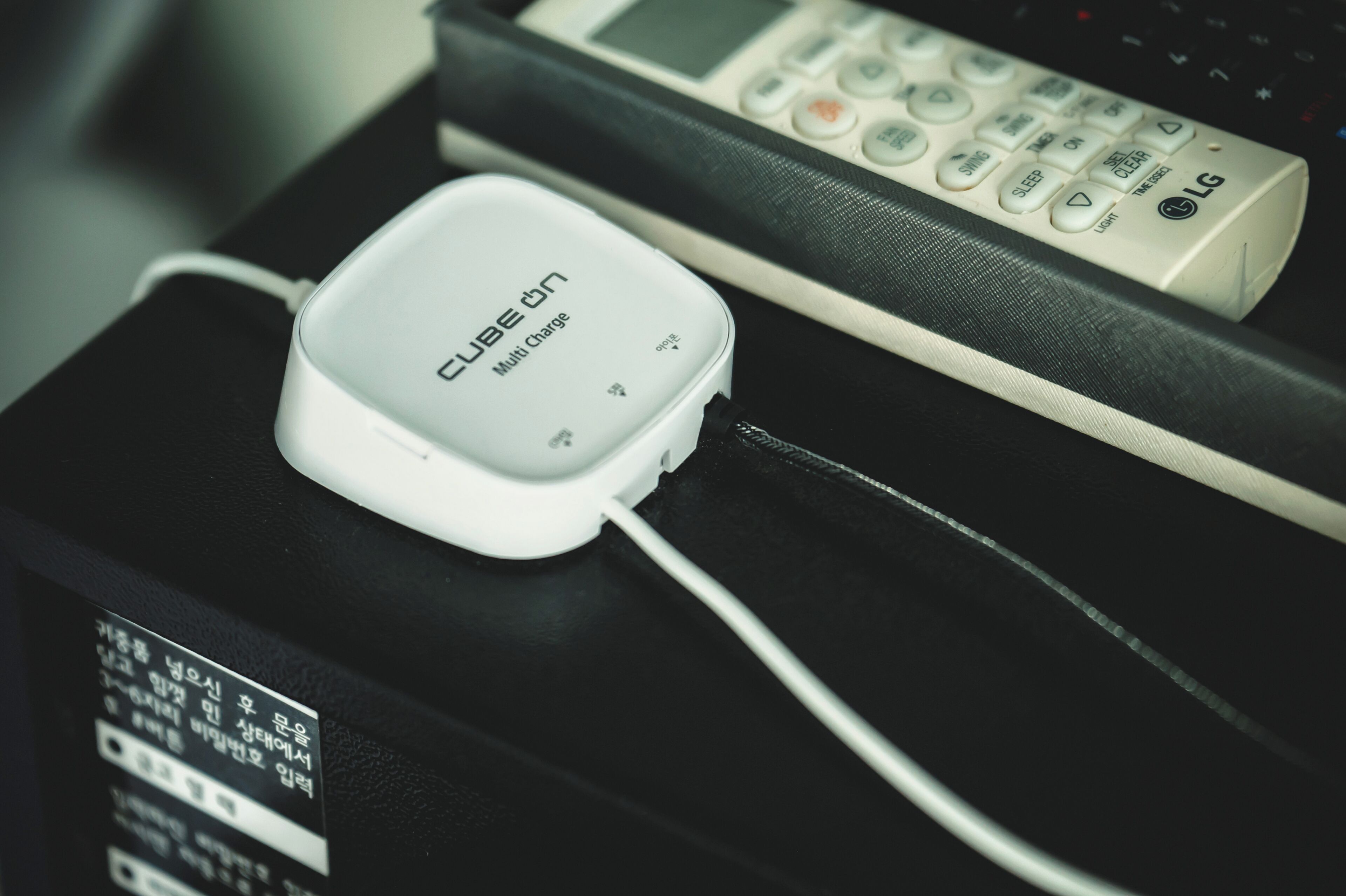 A white cube-shaped device labeled "Cube 6n Multi Charge" on a black surface, next to a remote control.