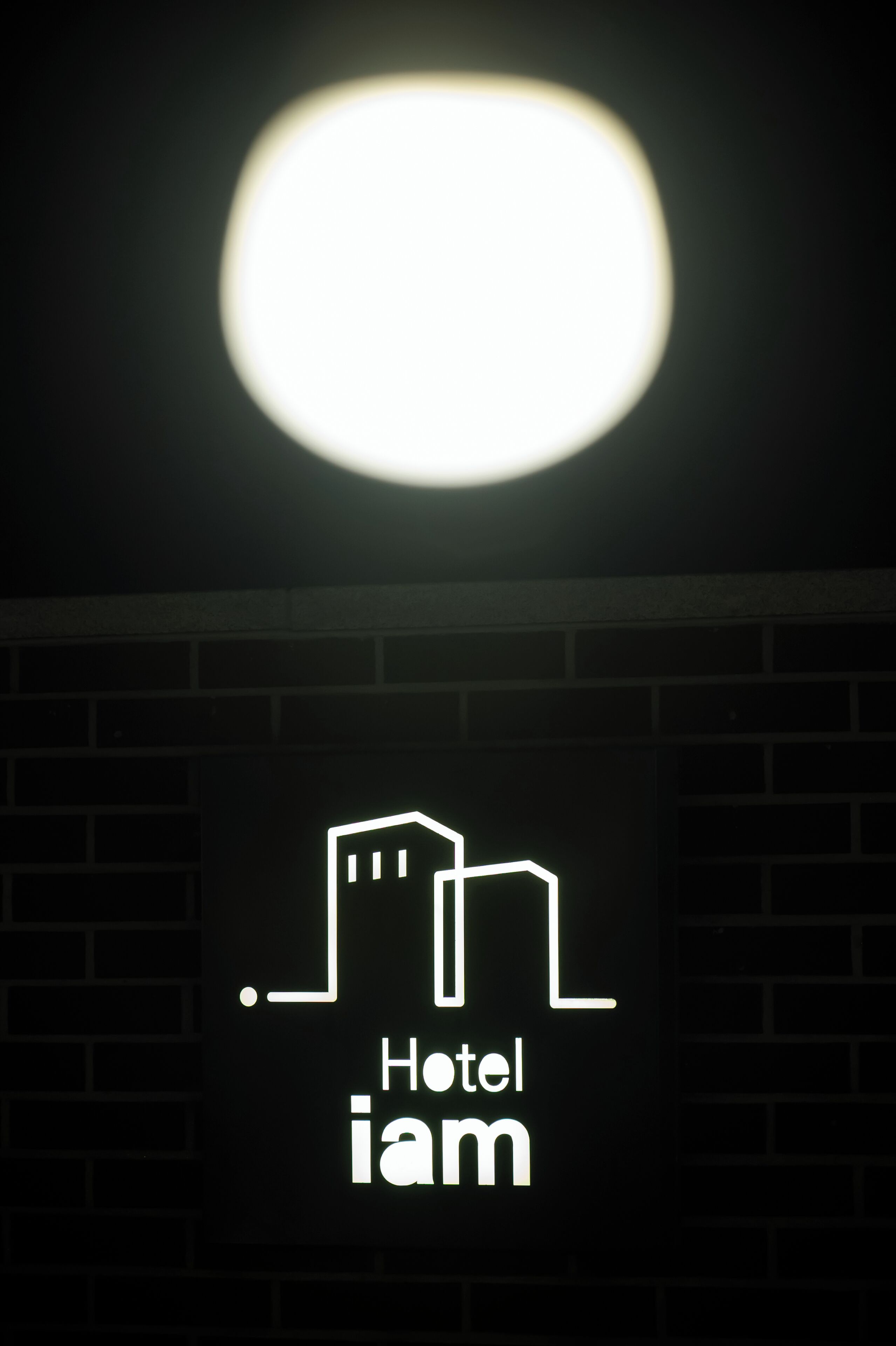Un letrero de neón con un icono de edificio y el texto "Hotel iam" sobre un fondo de pared de ladrillo.