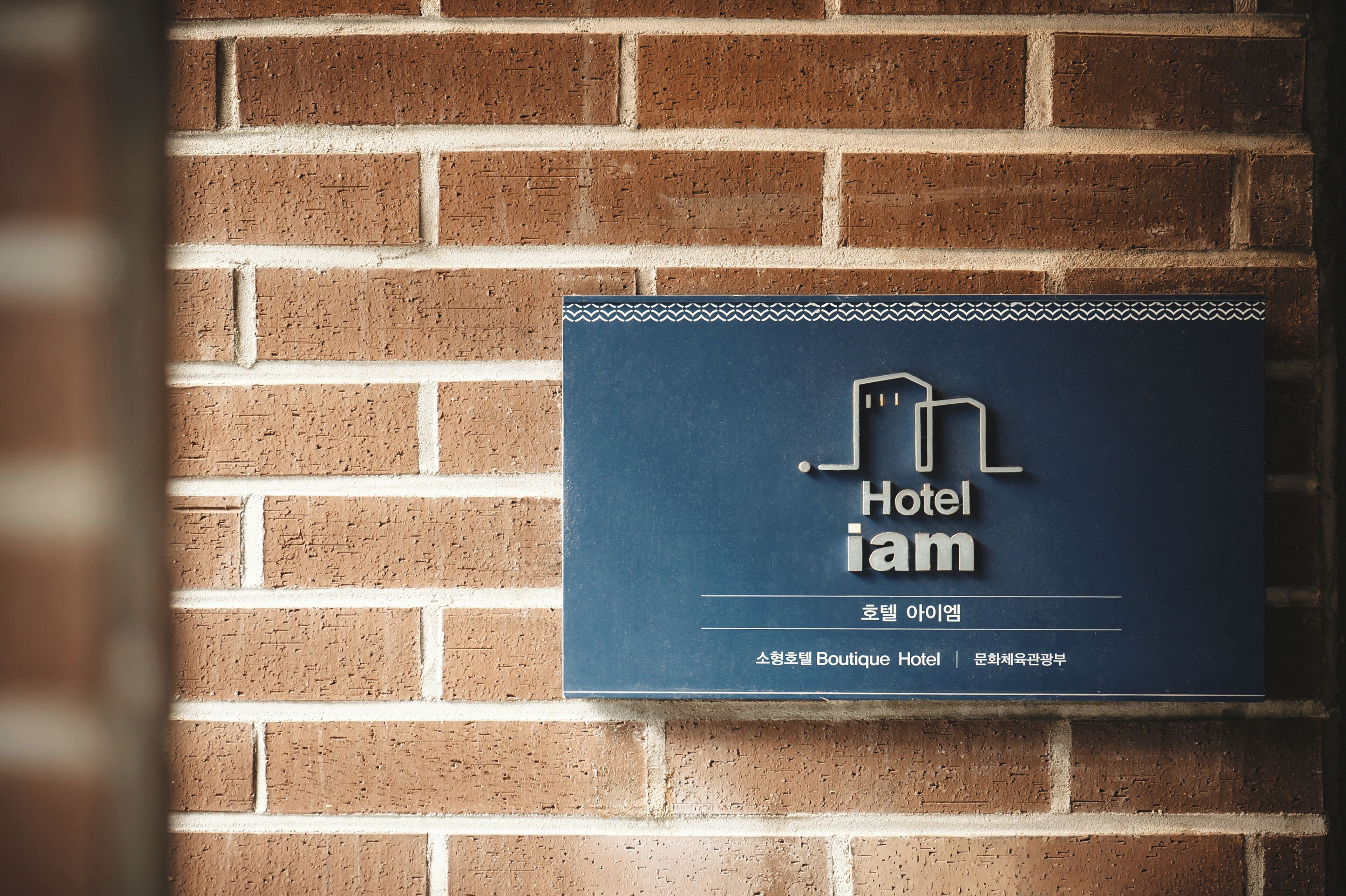 Un letrero en una pared de ladrillo para el Hotel iam, con un logotipo sencillo y texto que indica que es un hotel boutique.