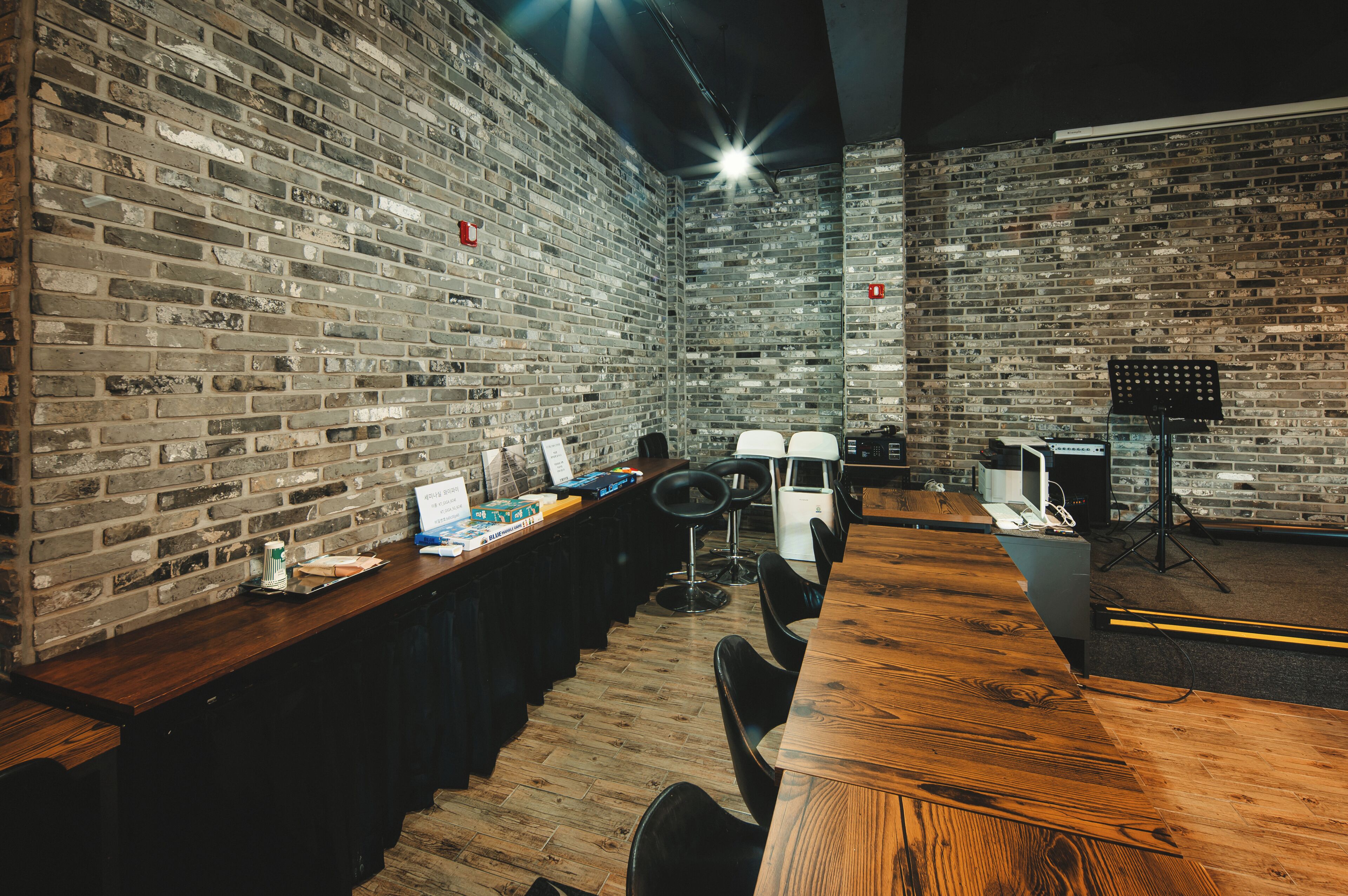 Een moderne bar met een bakstenen muur, een houten toonbank, barstoelen en een noteren standaard.