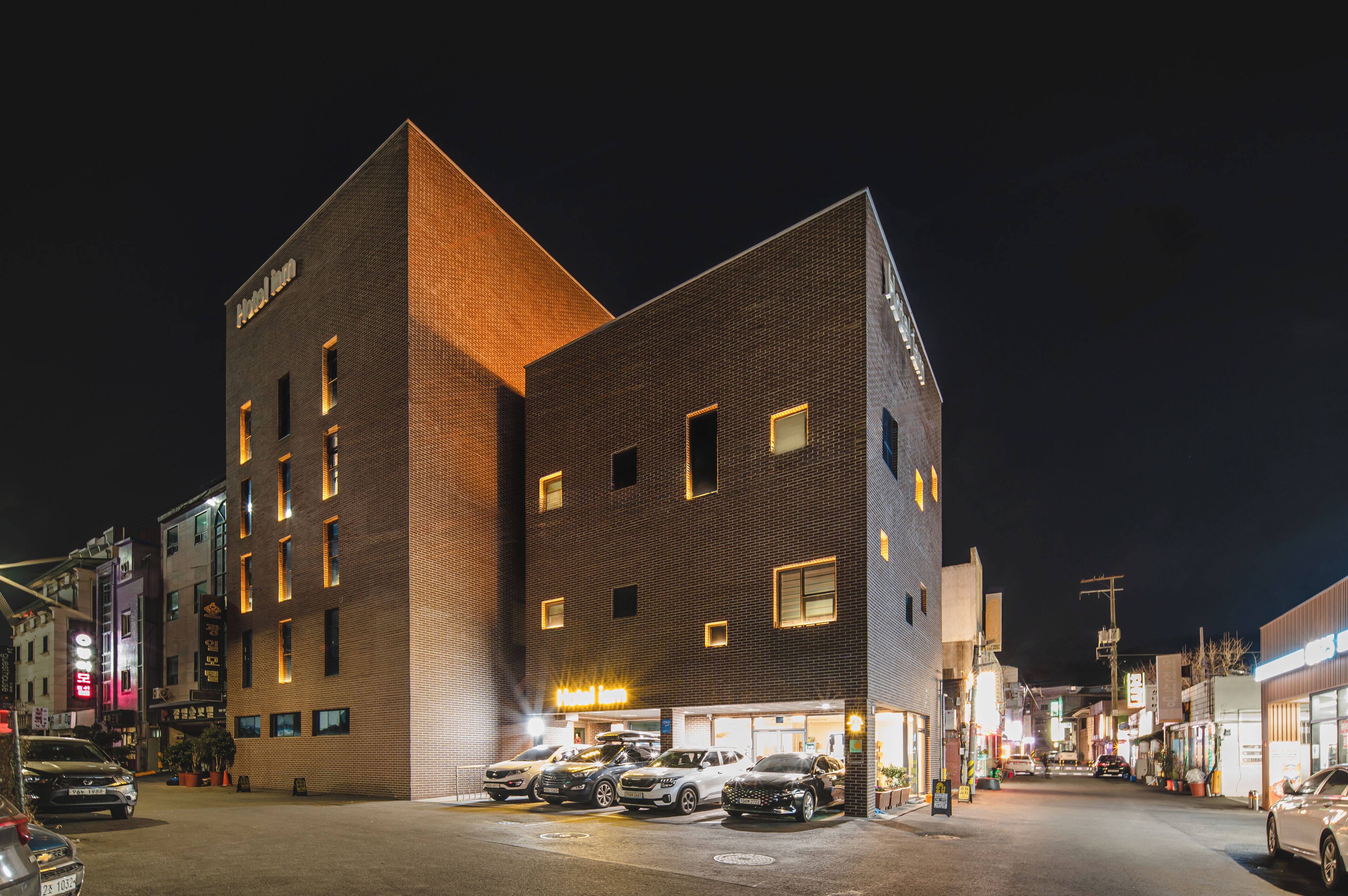 A multi-story hotel with a prominent corner design, multiple parking spaces, and a well-lit street at night.