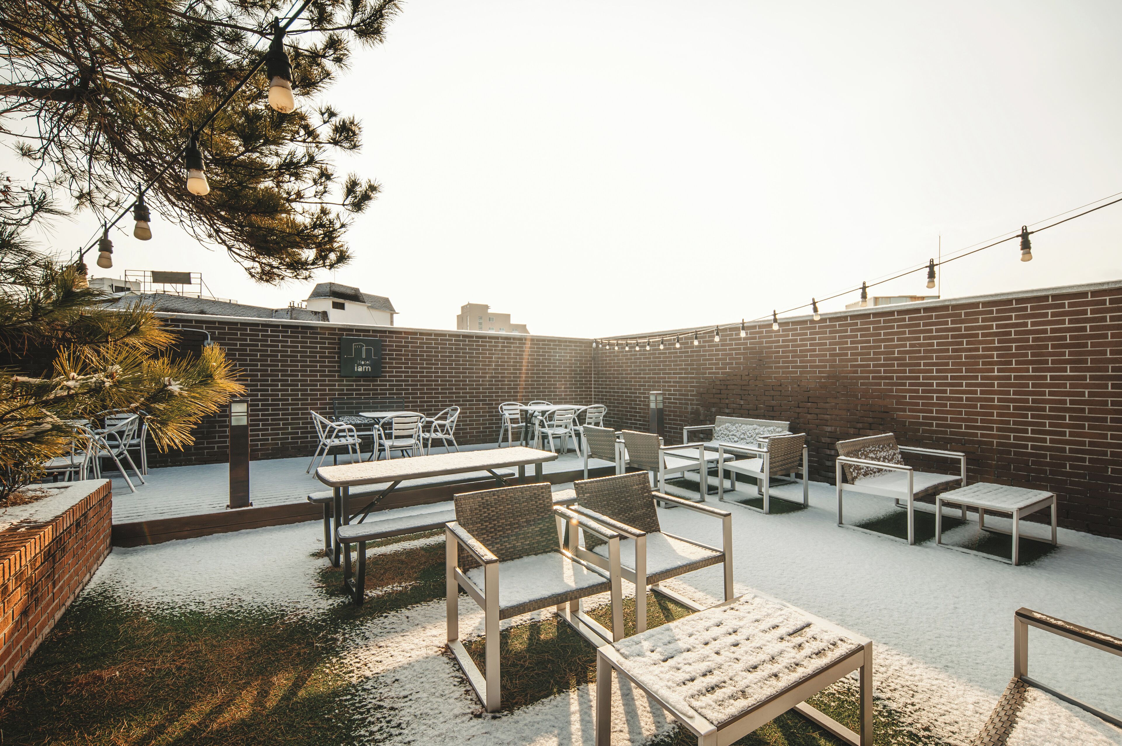 Un patio al aire libre con paredes de ladrillo, muebles blancos y luces colgantes.
