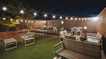 An outdoor patio area with brick walls, string lights, and outdoor furniture including tables and chairs.