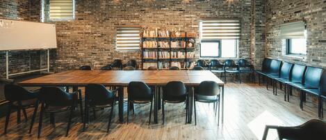 Una sala de conferencias con una larga mesa de madera, sillas negras, una estantería y una pizarra.