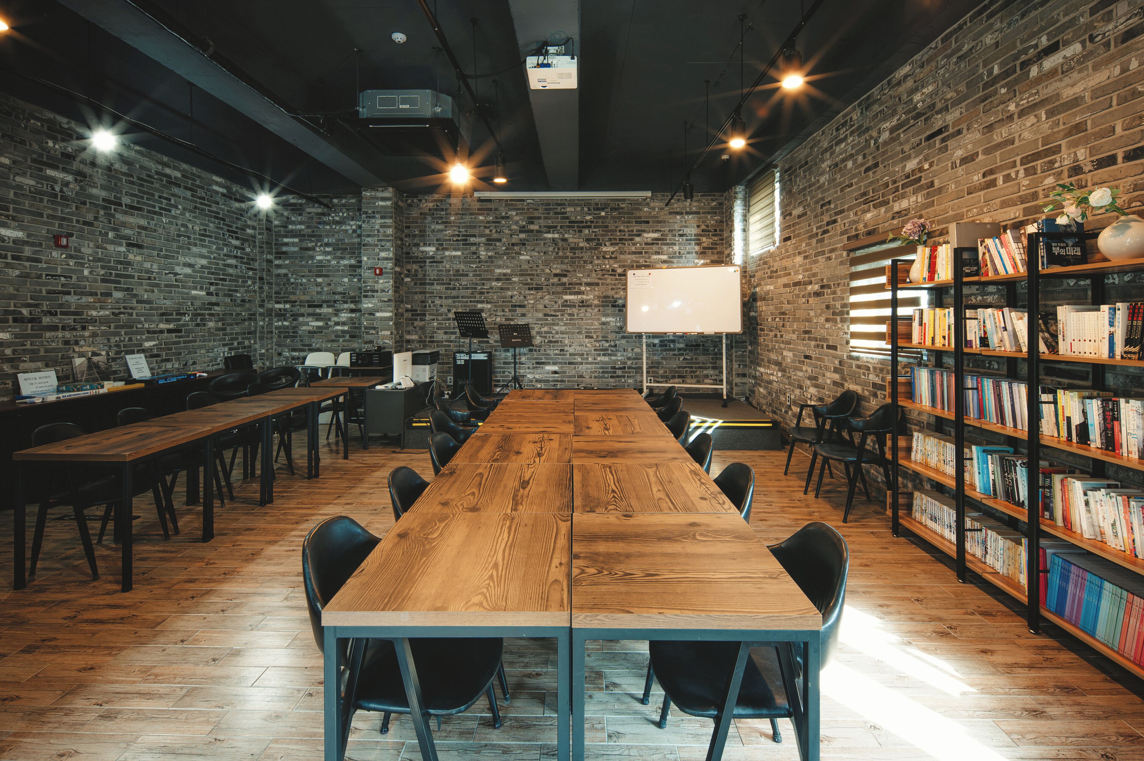 A conference room with a long wooden table, black chairs, a whiteboard, and a bookshelf filled with books.