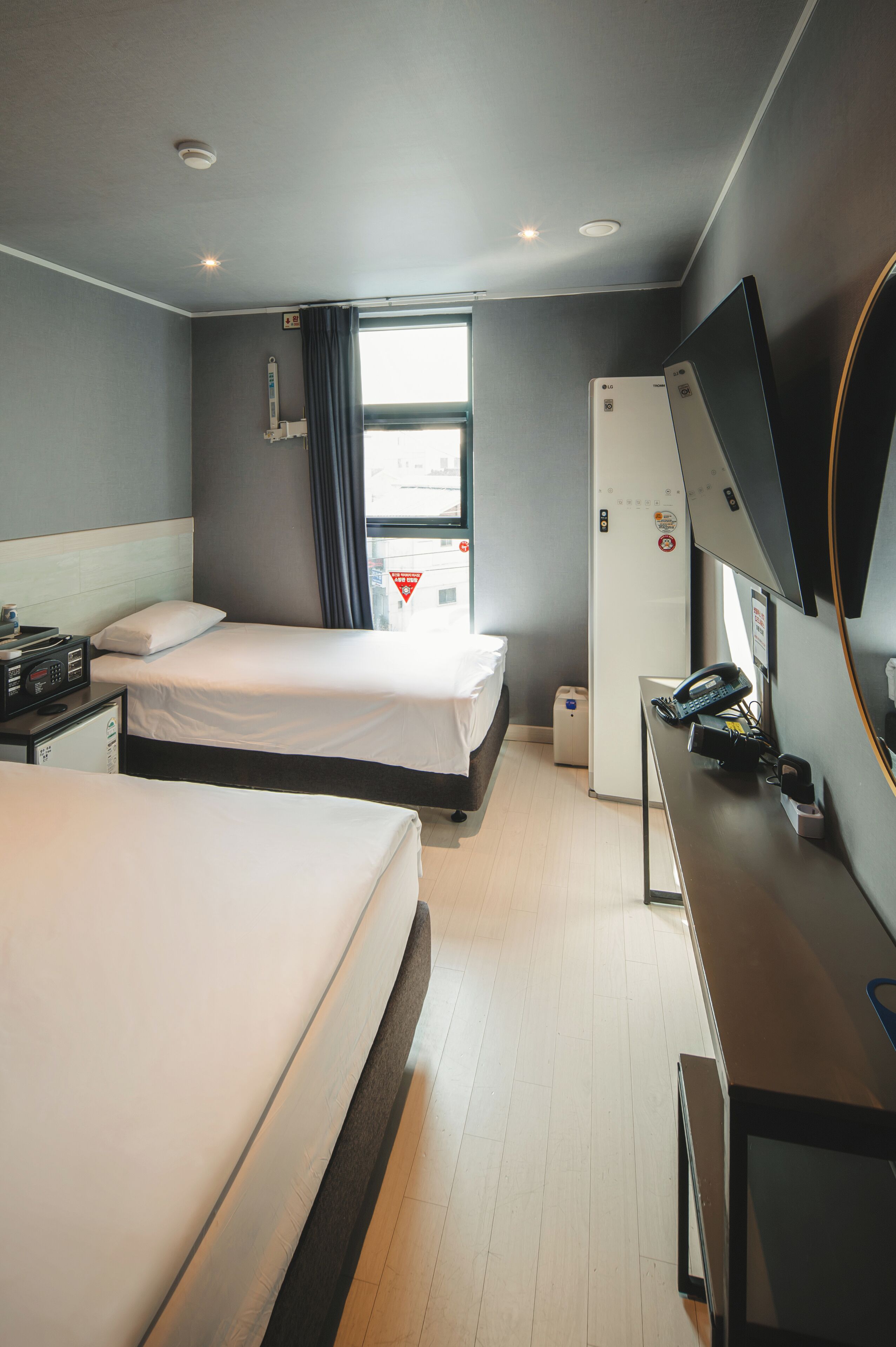 A hotel room with two beds, a desk with a telephone, a television, and a window with curtains.