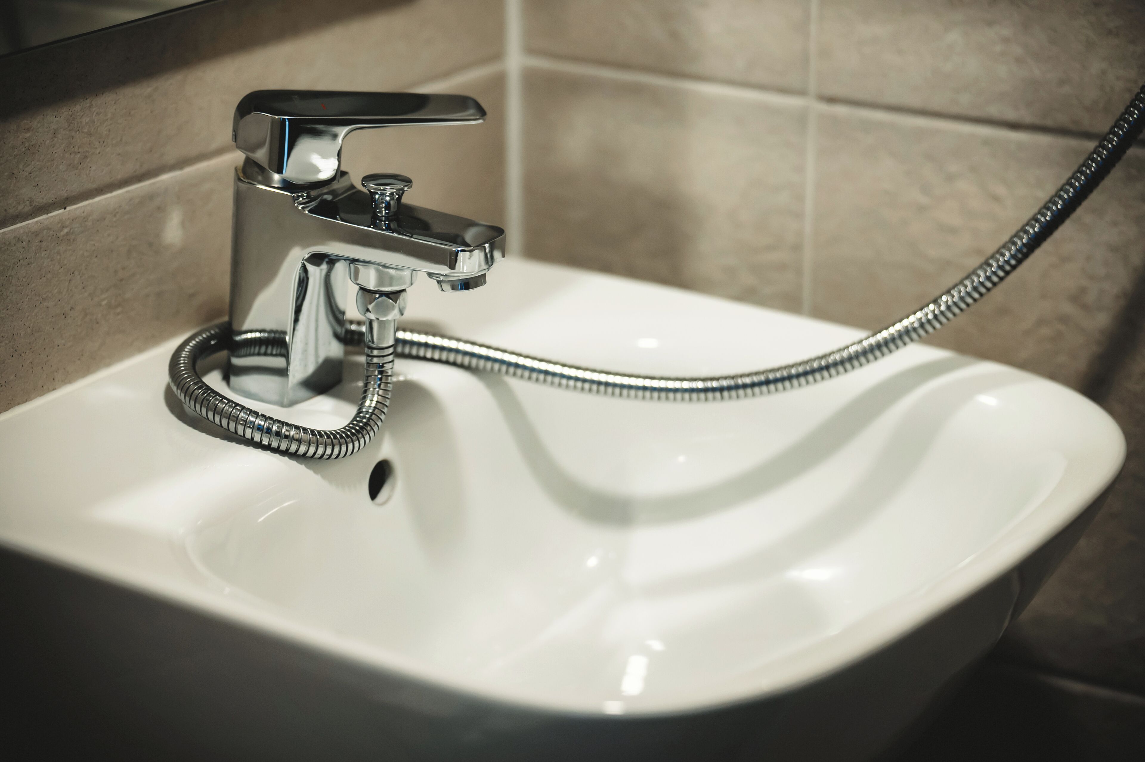 A bathroom sink with a chrome faucet and a flexible shower hose.