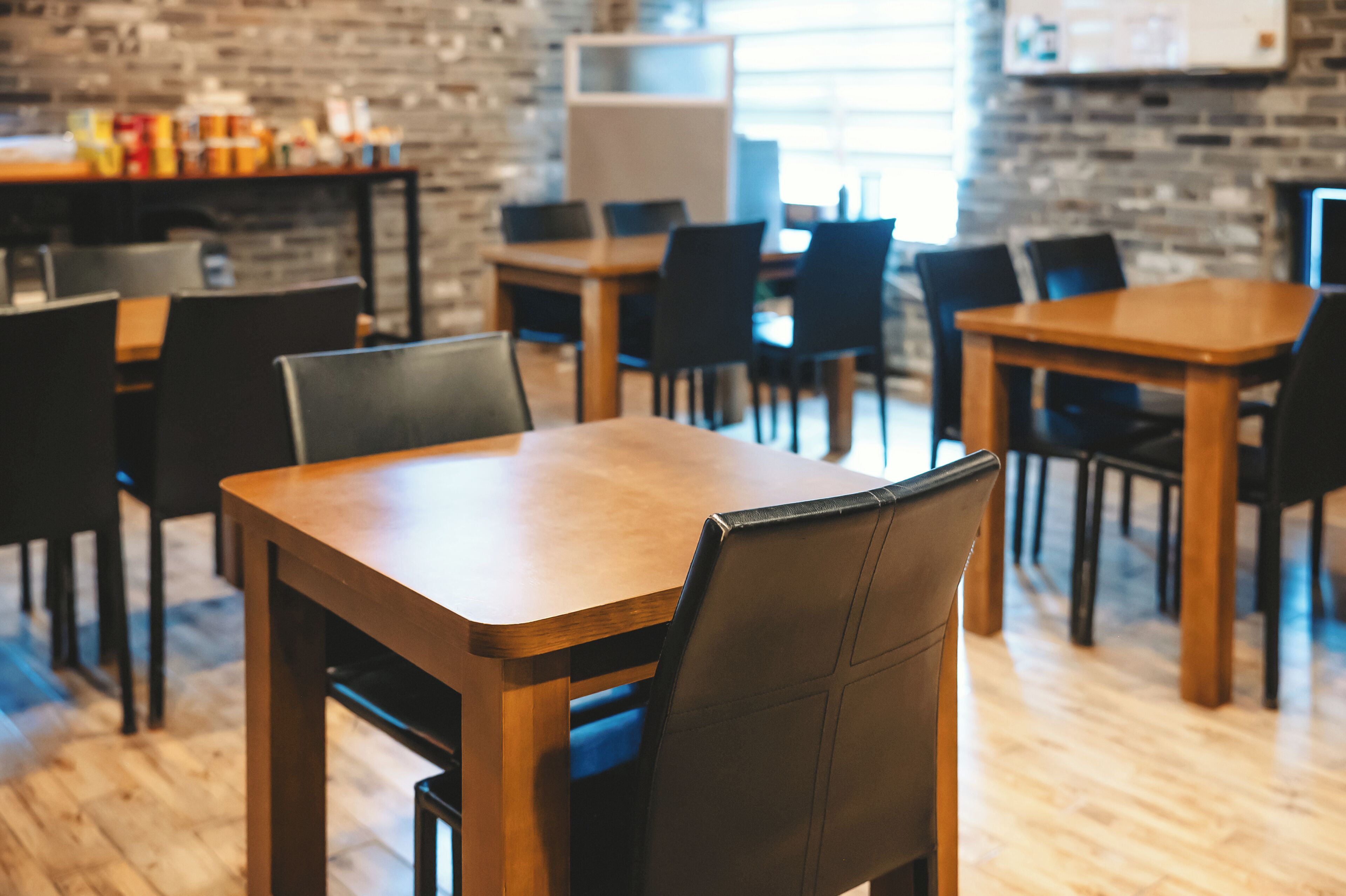 Un restaurant avec des tables en bois et des chaises noires, des murs en briques et un comptoir où sont exposés divers articles.