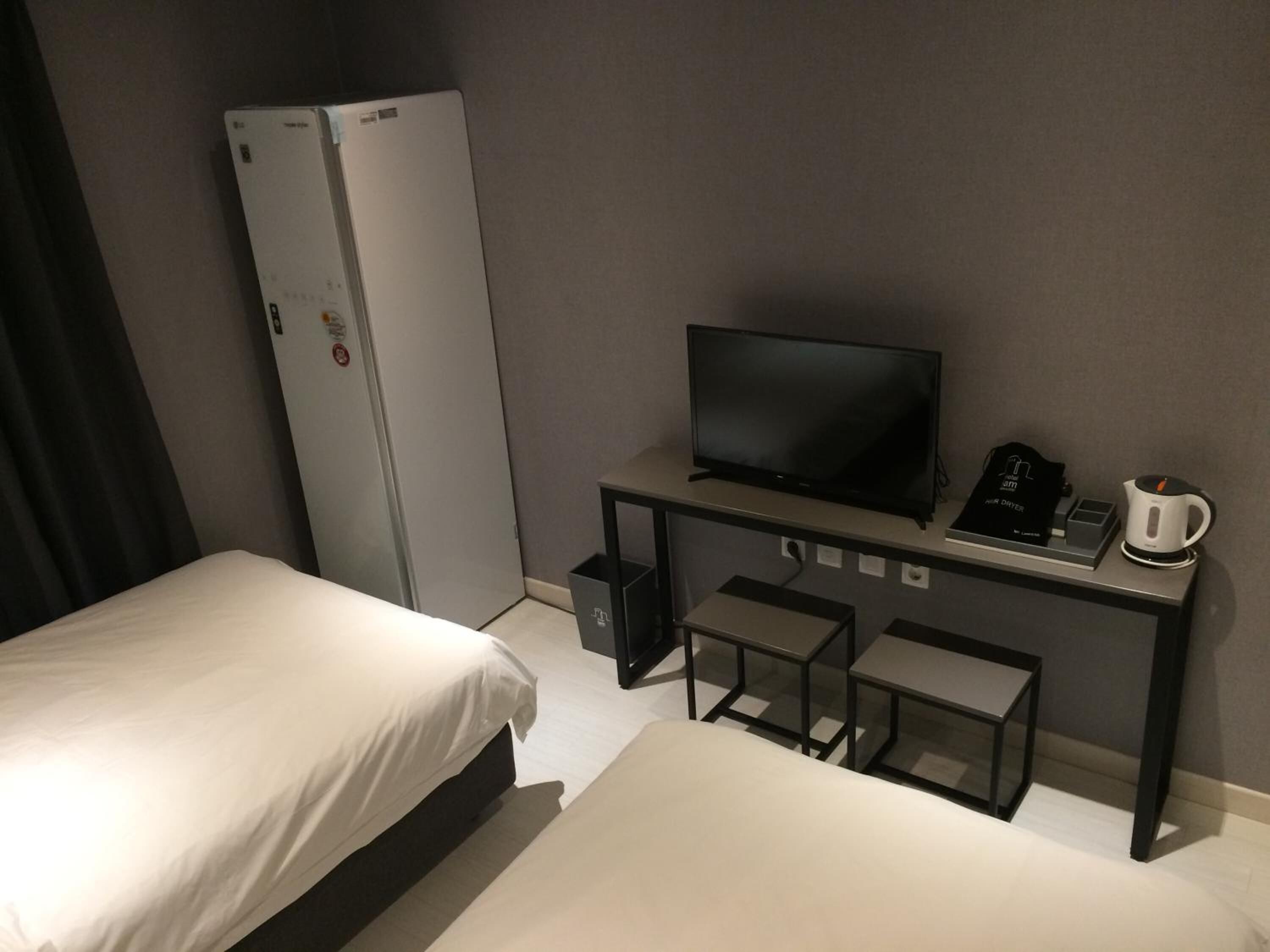 Habitación de hotel con dos camas, televisión, escritorio con cafetera y refrigerador.