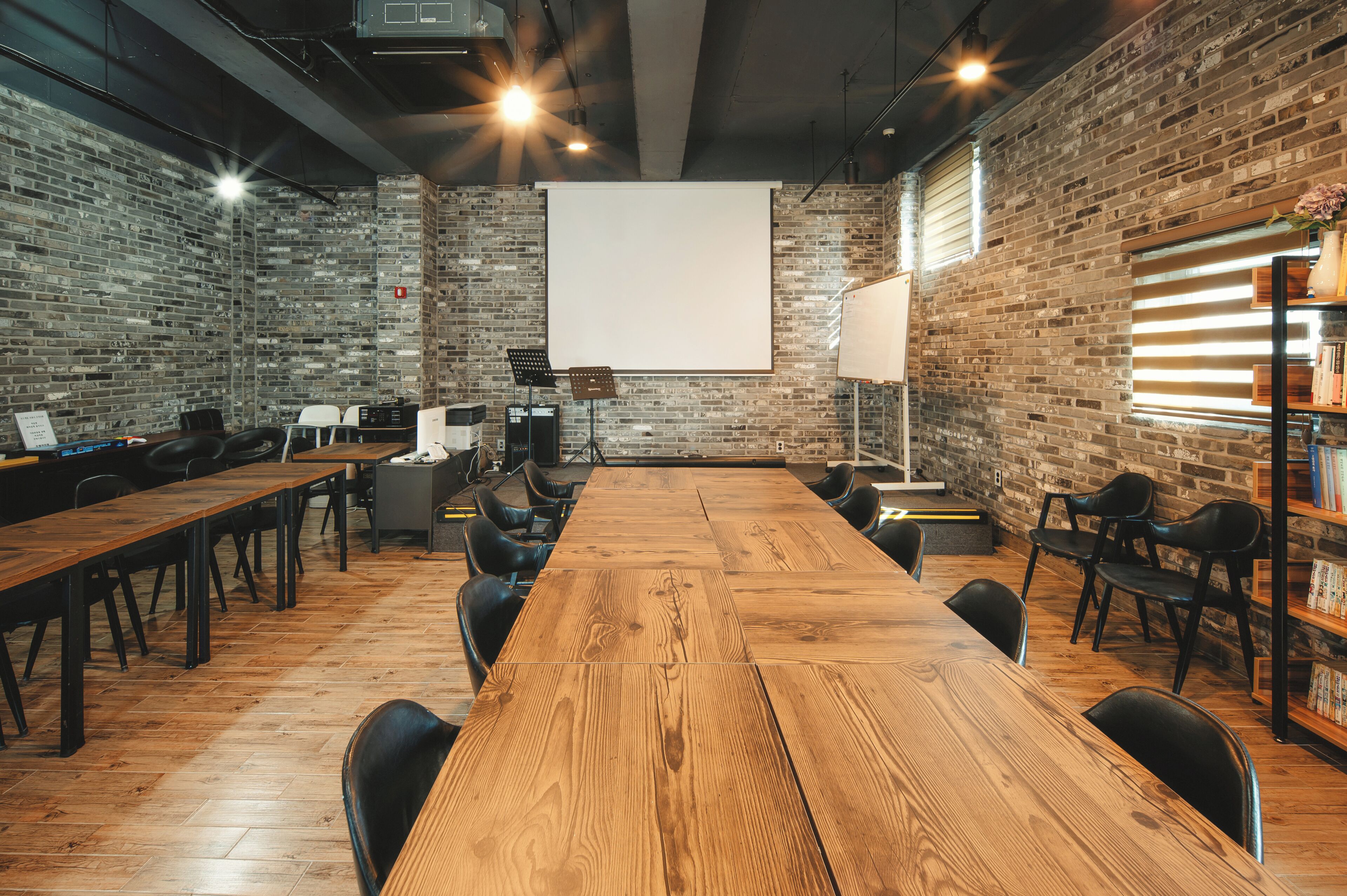 Una sala de conferències amb una taula de fusta llarga, cadires negres, una pantalla de projector i parets de rajola.