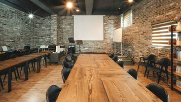 Una sala de conferències amb una taula de fusta llarga, cadires negres, una pantalla de projector i parets de rajola.