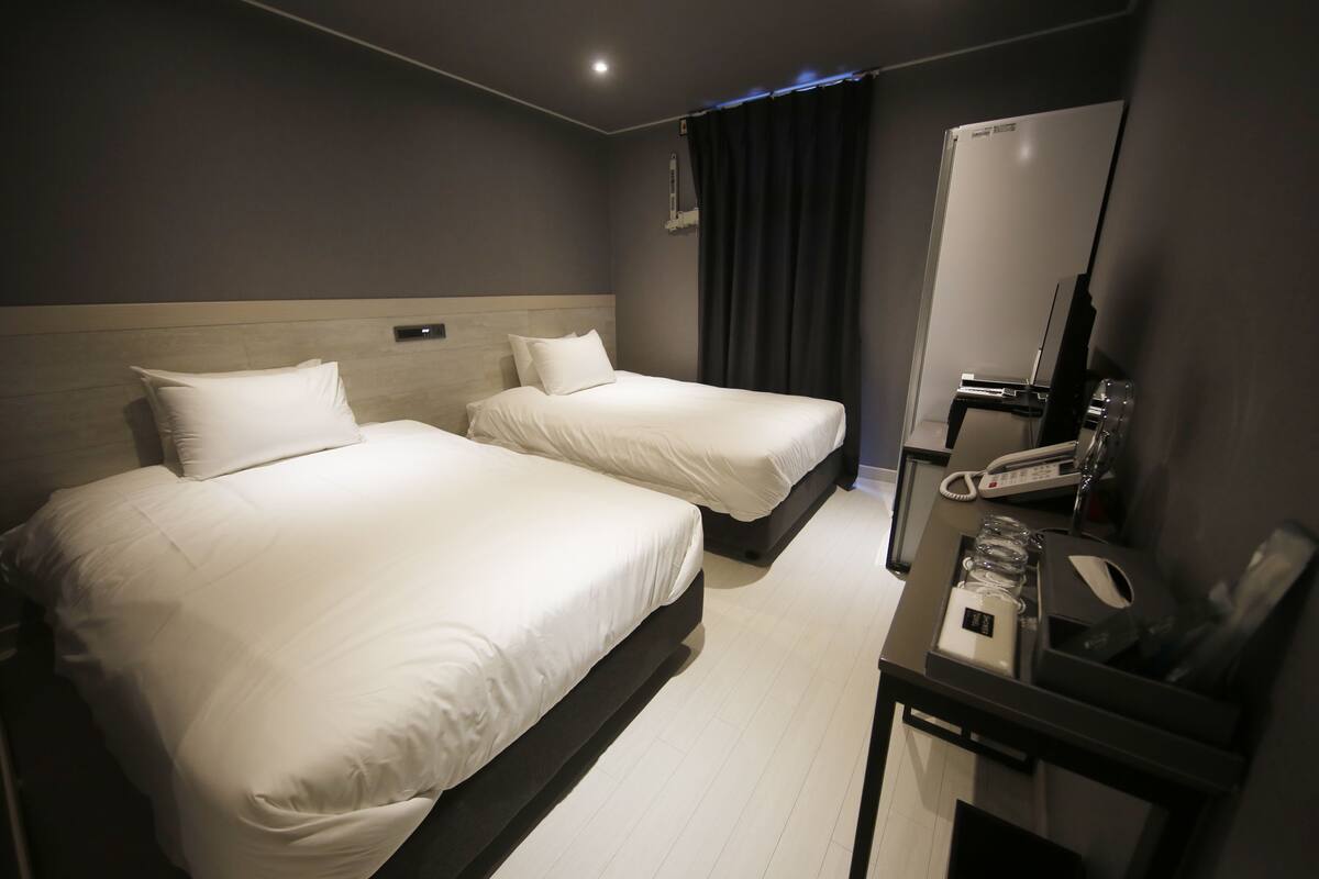 A hotel room with two beds, a desk with a telephone, and a mirror.