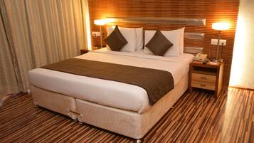 A hotel room with a large bed, wooden headboard, two bedside tables, a lamp, and a telephone.