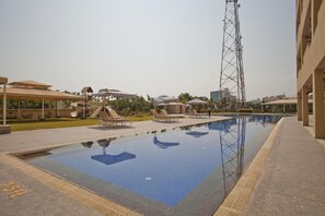 A swimming pool with lounge chairs and umbrellas, surrounded by buildings and a tall communication tower. - St Laurn - The Spiritual Resort (Rahata)