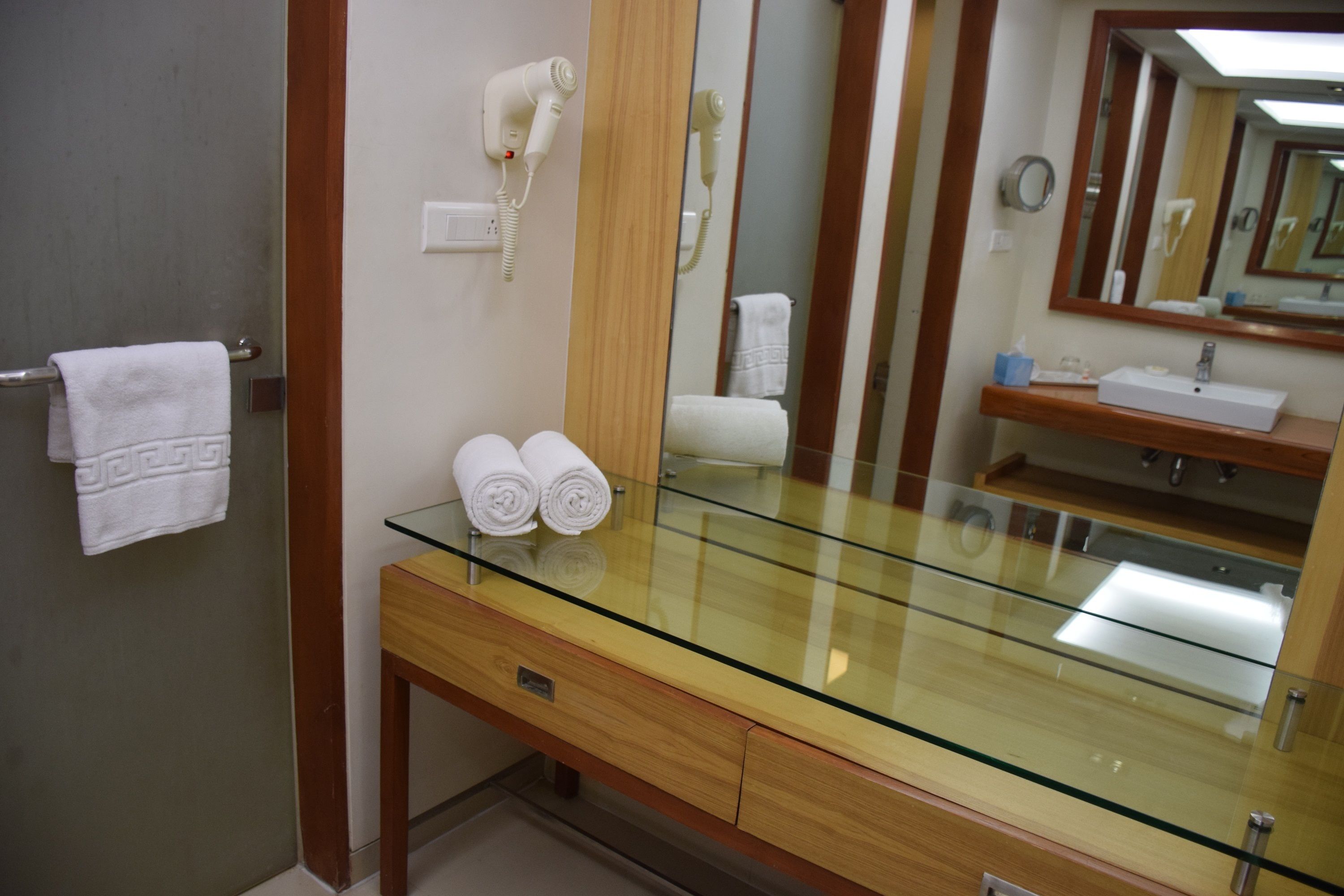 Un baño con tocador de superficie de vidrio, un perchero, un secador de pelo y un espejo.