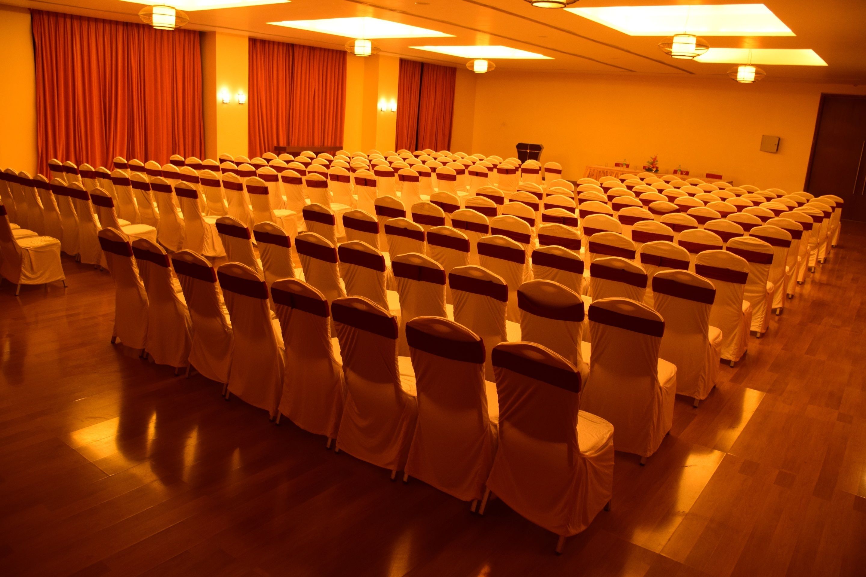 A conference room with rows of chairs, a stage, and curtains.