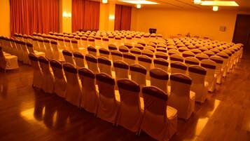 Un salón de conferencias con filas de sillas, un escenario y cortinas.