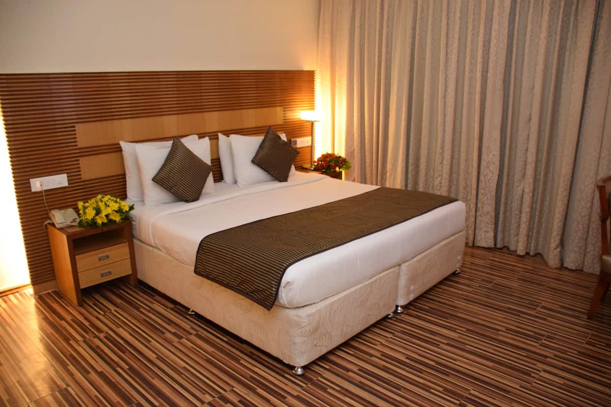 Een hotelkamer met een groot bed, een houten hoofdbord, een nachtkastje met een lamp en een raam met gordijnen.