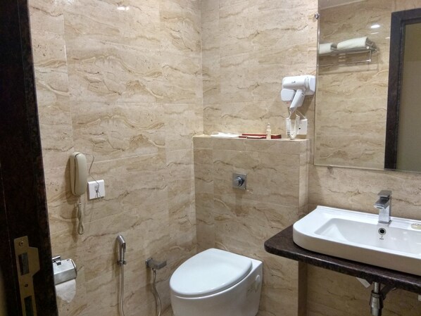 Un baño con pared de mármol, inodoro blanco, lavabo con espejo y secador de pelo en la pared.