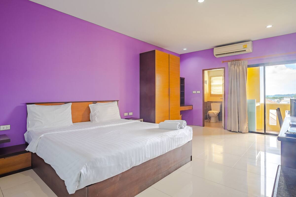 A modern bedroom with a large bed, purple walls, and a view of the outside.