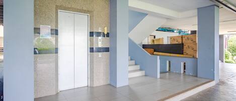 Un interior espacioso con una escalera que conduce a un nivel superior, una puerta con un letrero y un piso de baldosas.