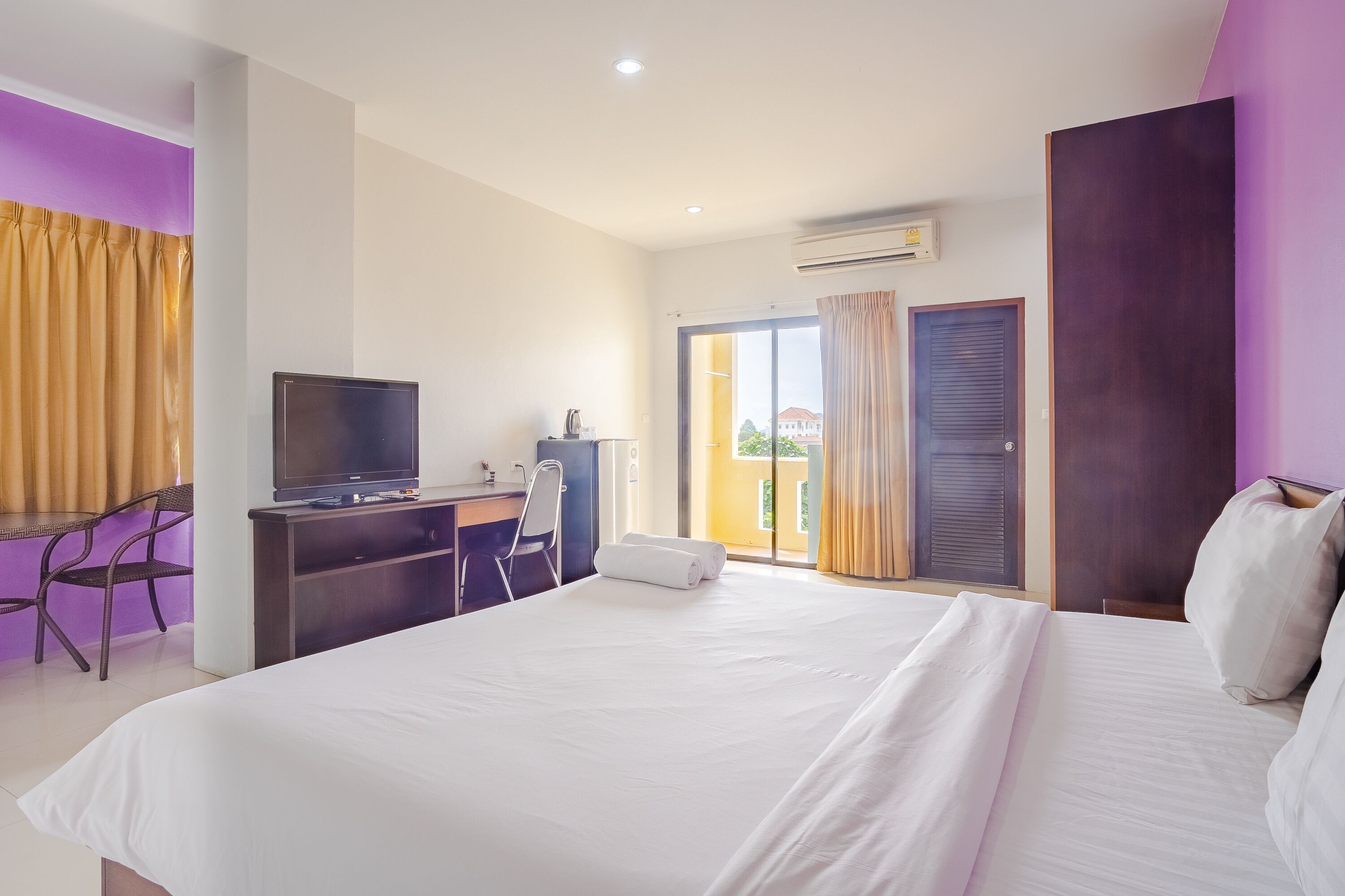 Une chambre d’hôtel avec un lit, un bureau avec un ordinateur, une télévision et une fenêtre avec des rideaux.