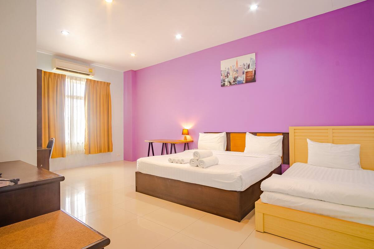A hotel room with a large bed, a desk, a chair, and a small table with a lamp.