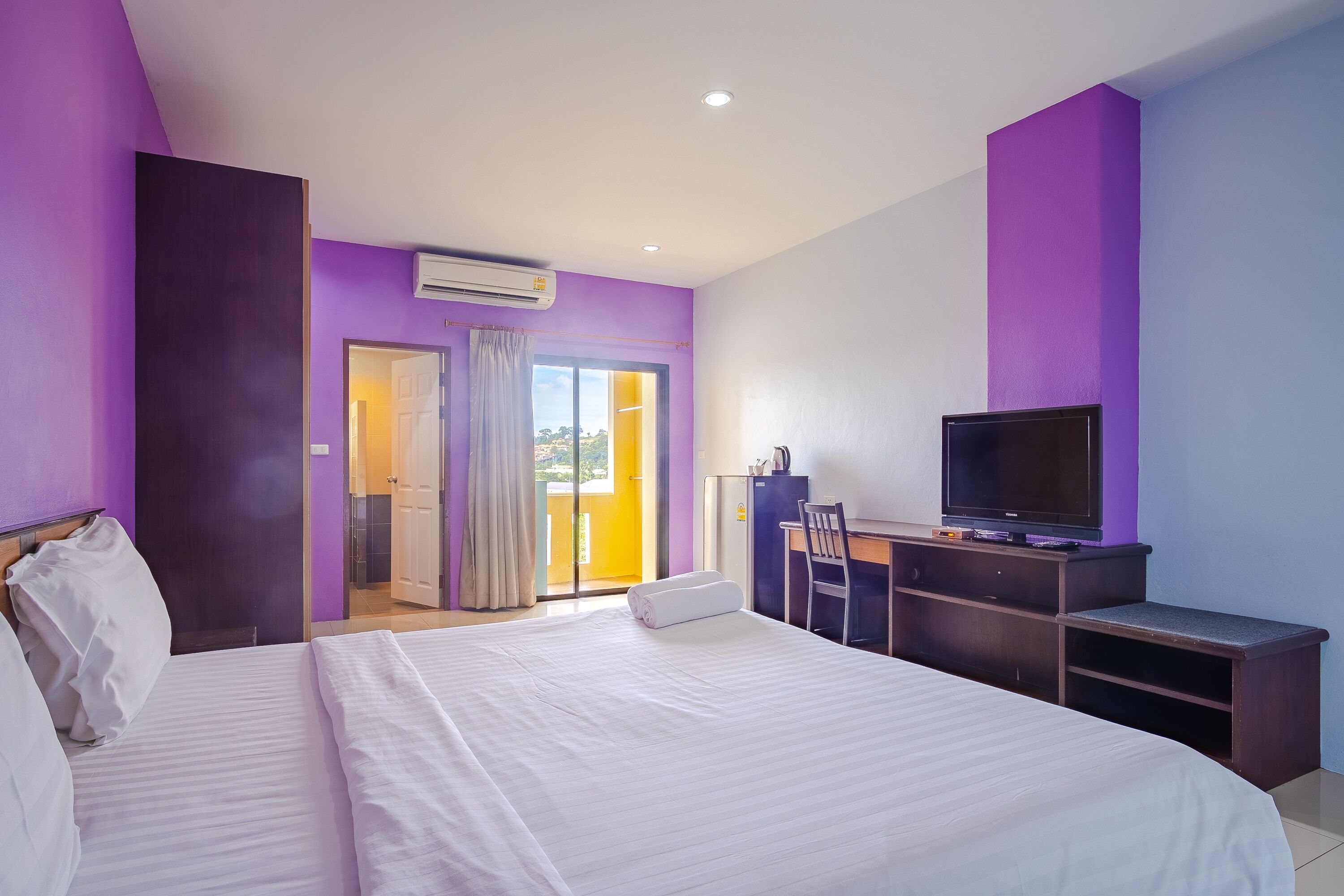 A hotel room with a large bed, a desk with a television, and an air conditioning unit on the wall.