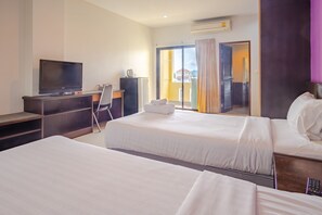 A hotel room with two beds, a desk with a television, a chair, and a view of a building through a glass door. - AJ Residence (Ratsada)