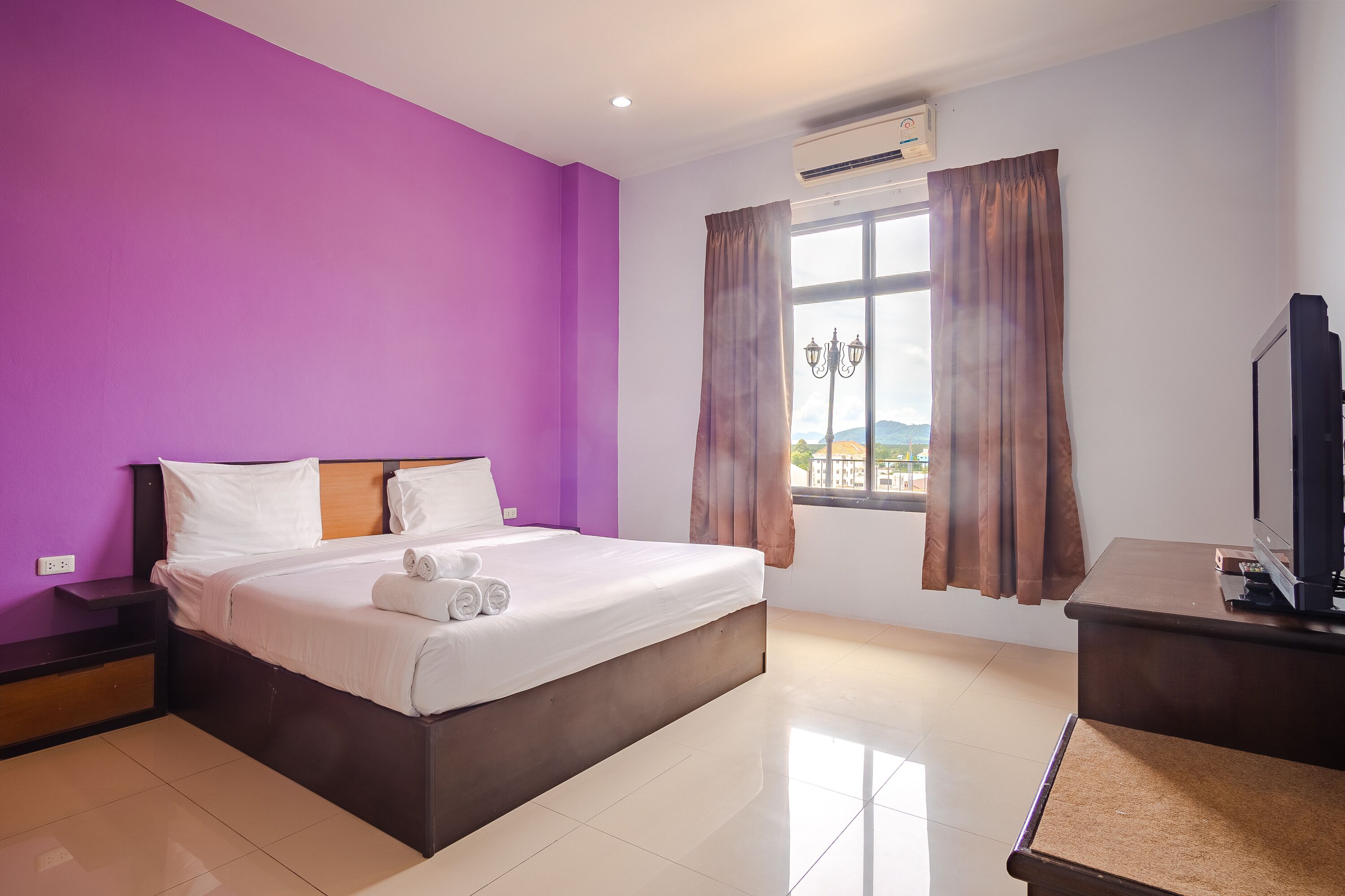 Una habitación de hotel con cama, televisión, escritorio y ventana con cortinas.