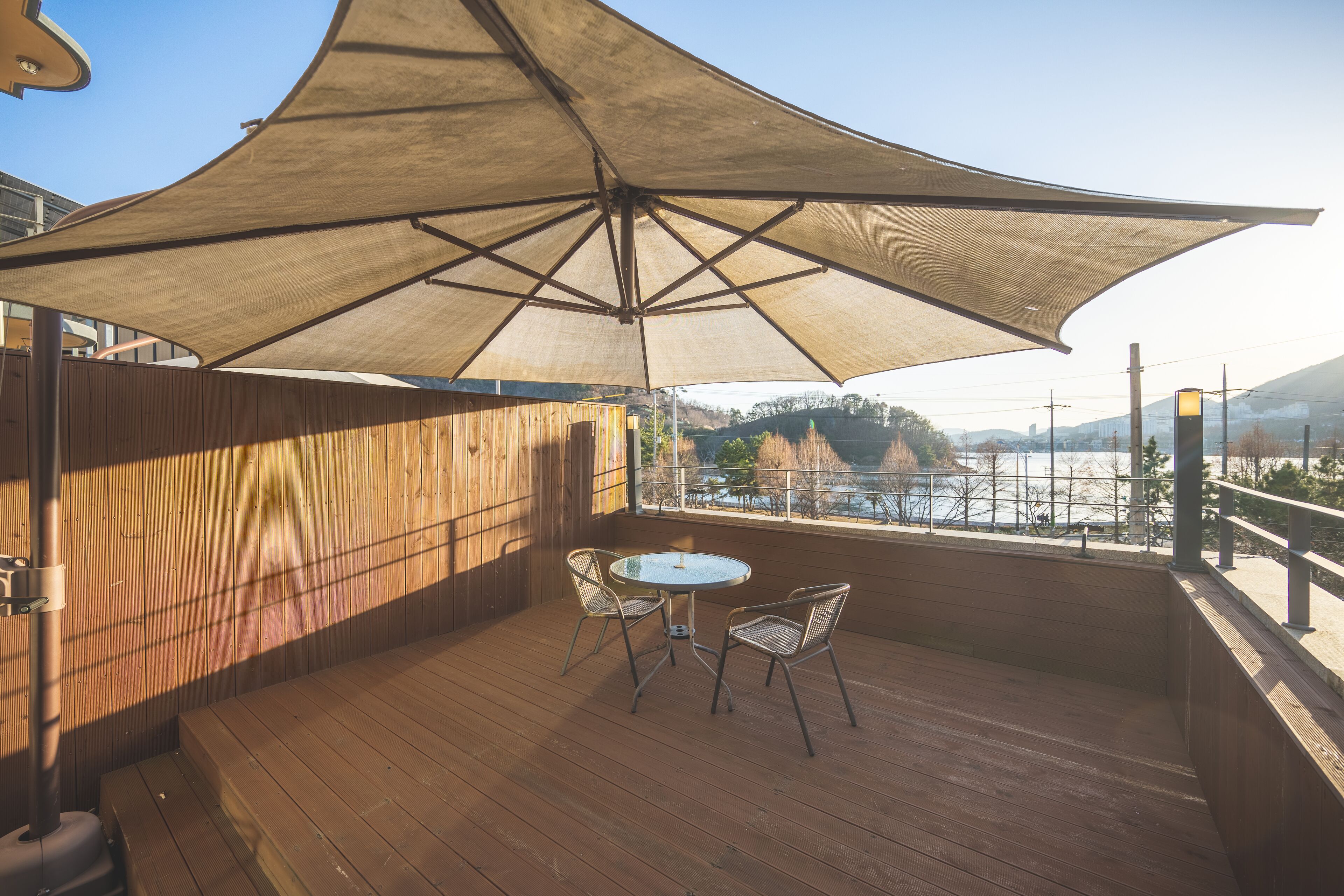 A wooden deck with a table and chairs under a large umbrella, overlooking a scenic view.