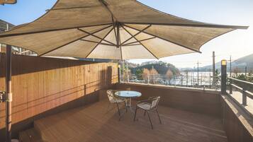 A wooden deck with a table and chairs under a large umbrella, overlooking a scenic view.