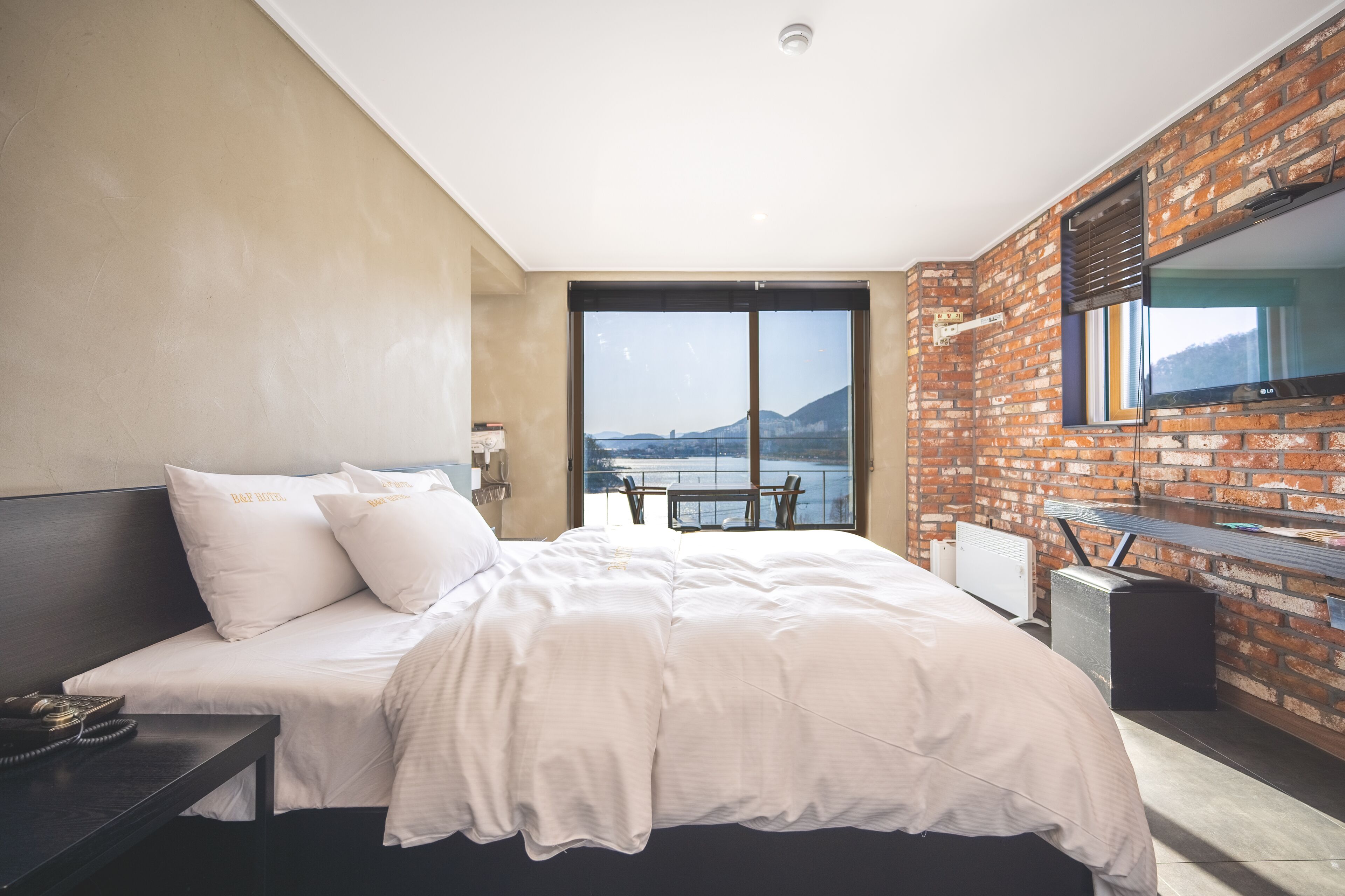 A modern hotel room with a large bed, a desk, and a view of a body of water.