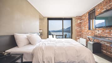 A modern hotel room with a large bed, a desk, and a view of a body of water.