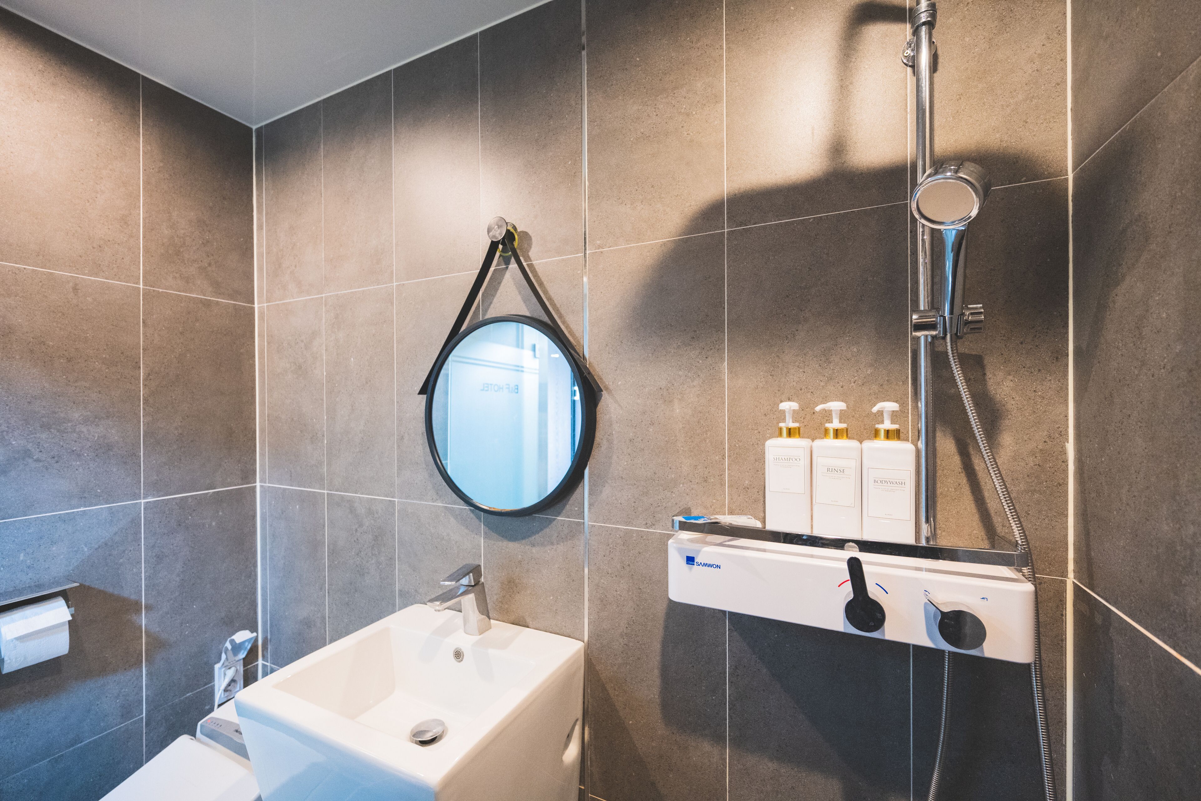 A modern bathroom with a white sink, a mirror, and a shower unit with controls.