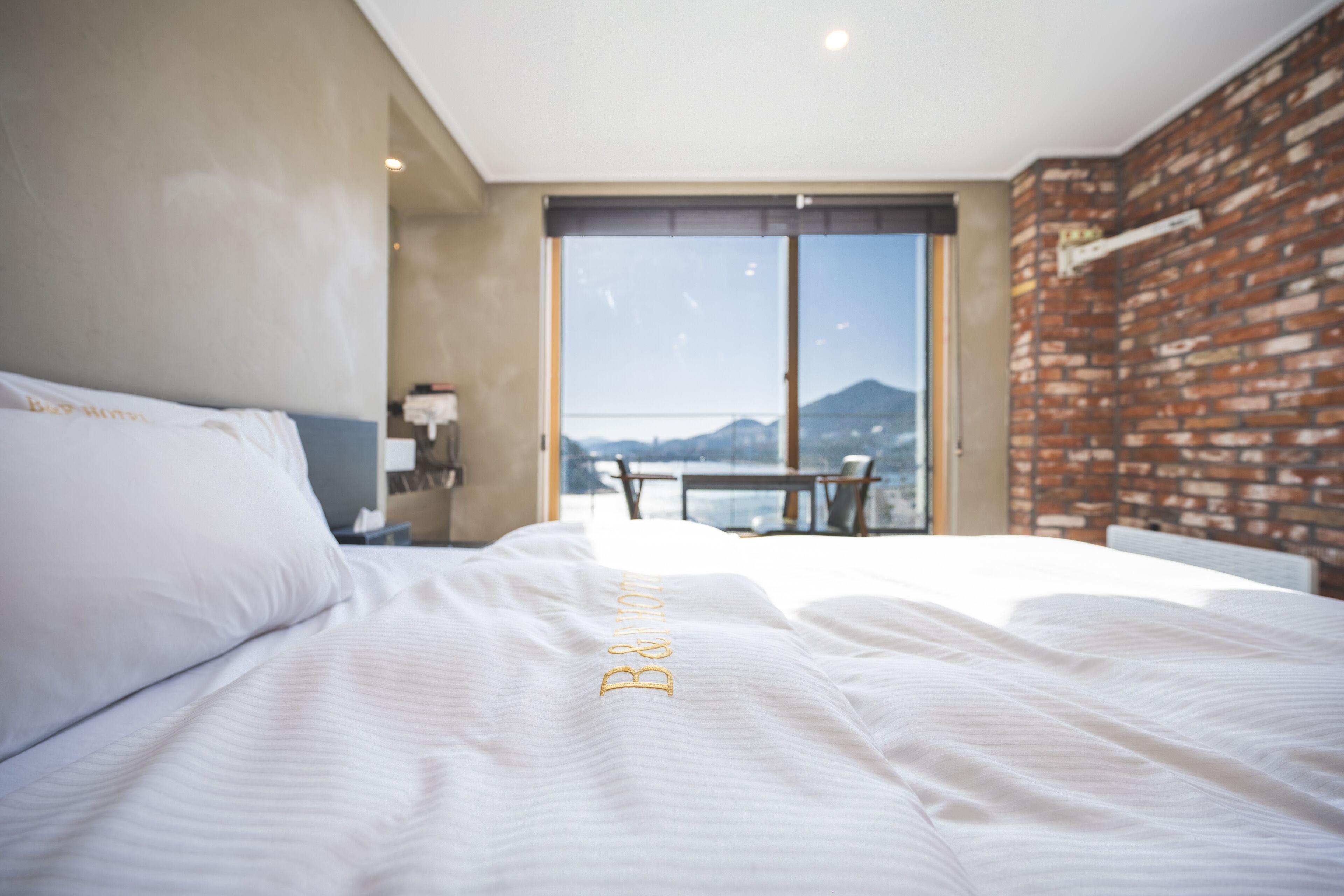 Quarto de hotel com uma cama grande, uma escrivaninha e vista para as montanhas através de uma porta de vidro.