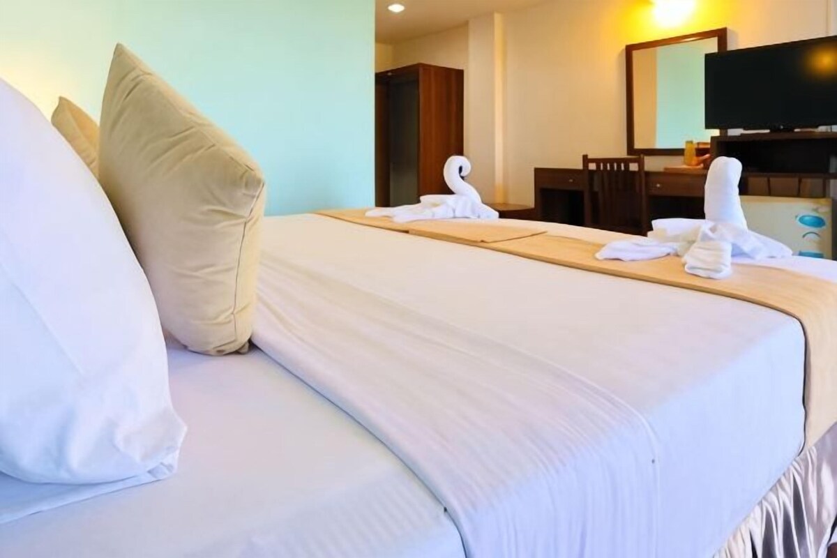 A hotel room with a bed, pillows, a wooden headboard, a desk with a chair, a television, and a mirror.