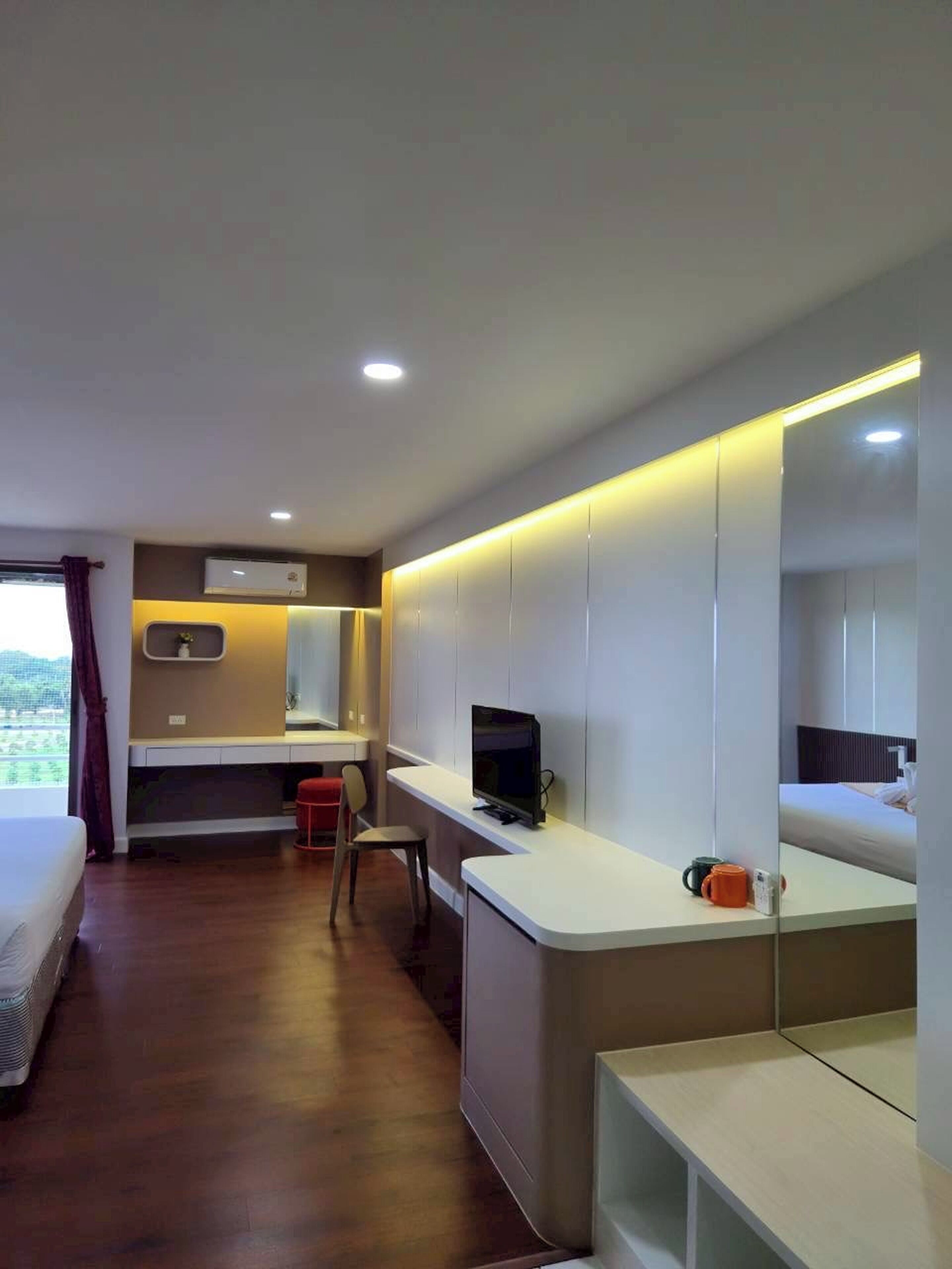 A modern hotel room with a bed, a desk with a computer, a TV, and a large mirror.