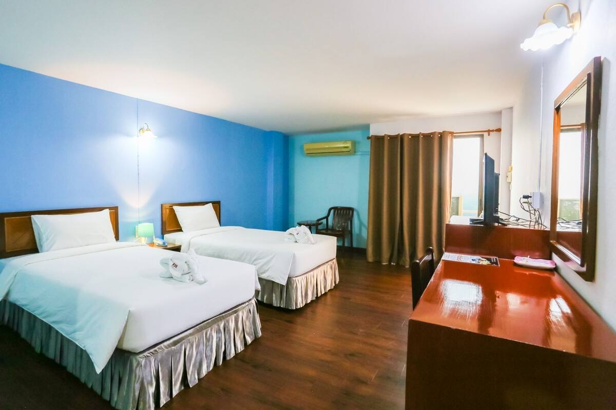 Ein Hotelzimmer mit zwei Betten, einem Schreibtisch, einem Stuhl und einem großen Spiegel.