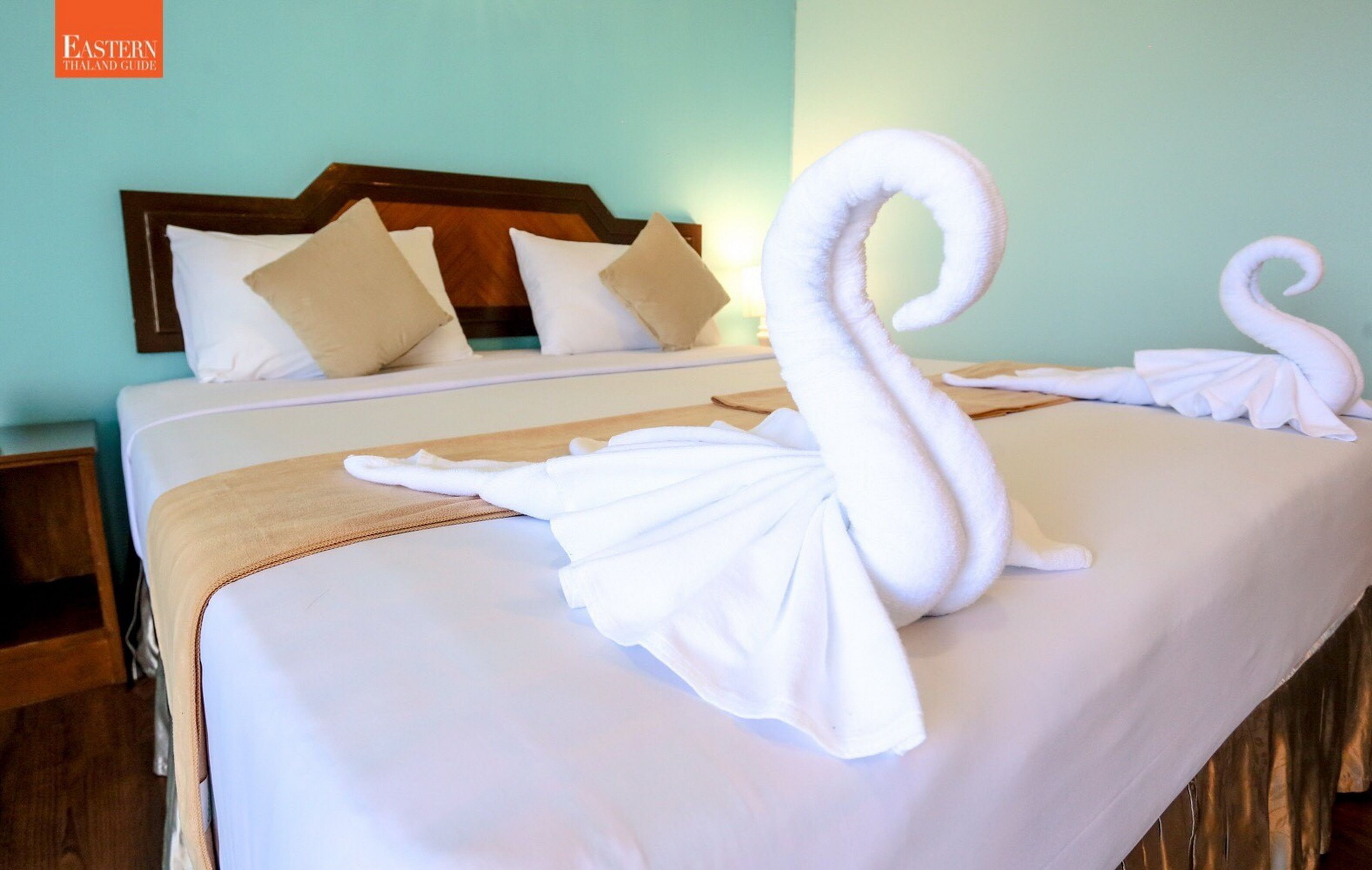Una habitación de hotel con una cama bien hecha, un cabecero de madera y una mesita de noche fijada a la pared.